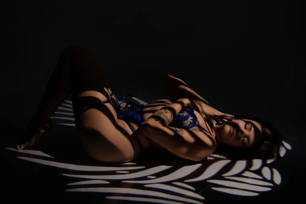 Femme en lingerie bleue allongée sous un jeu d'ombres rayées, séance boudoir en studio - Cindy Poulet photographe