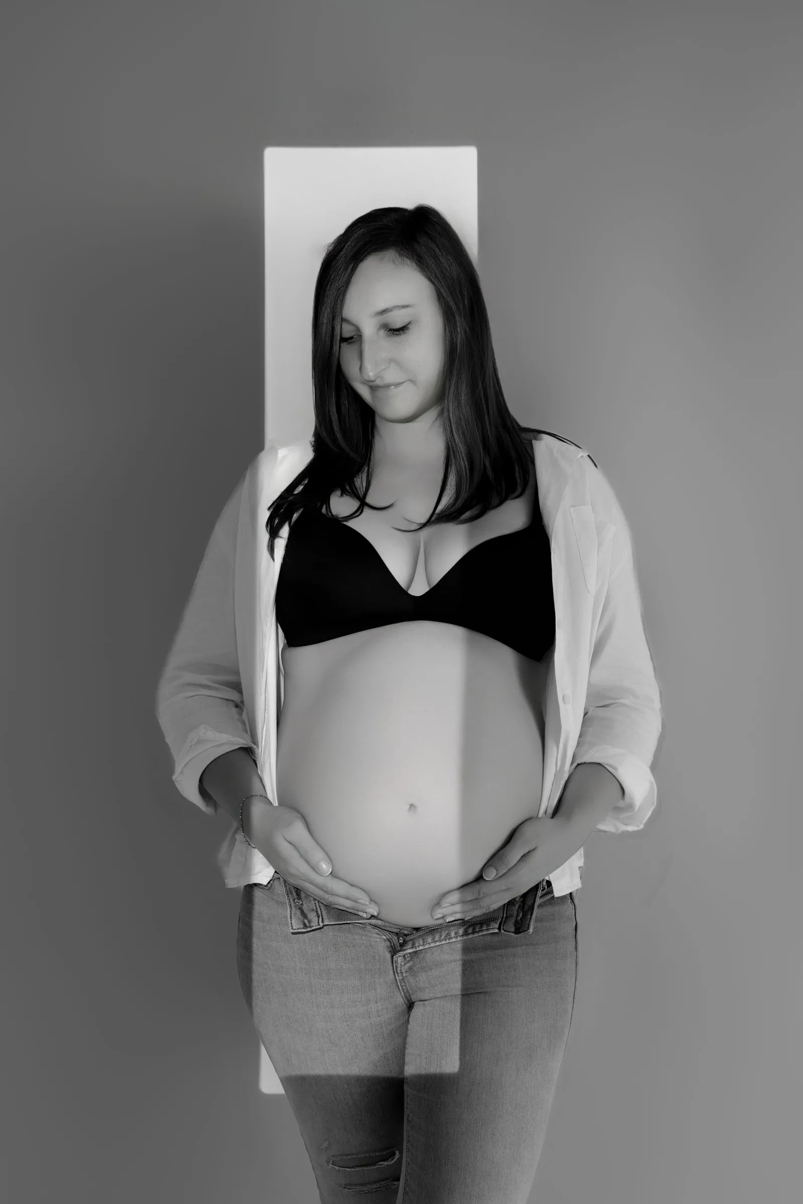 Portrait intimiste en noir et blanc d'une femme enceinte, mains sur son ventre rond, séance photo de grossesse par Cindy Poulet Photographe