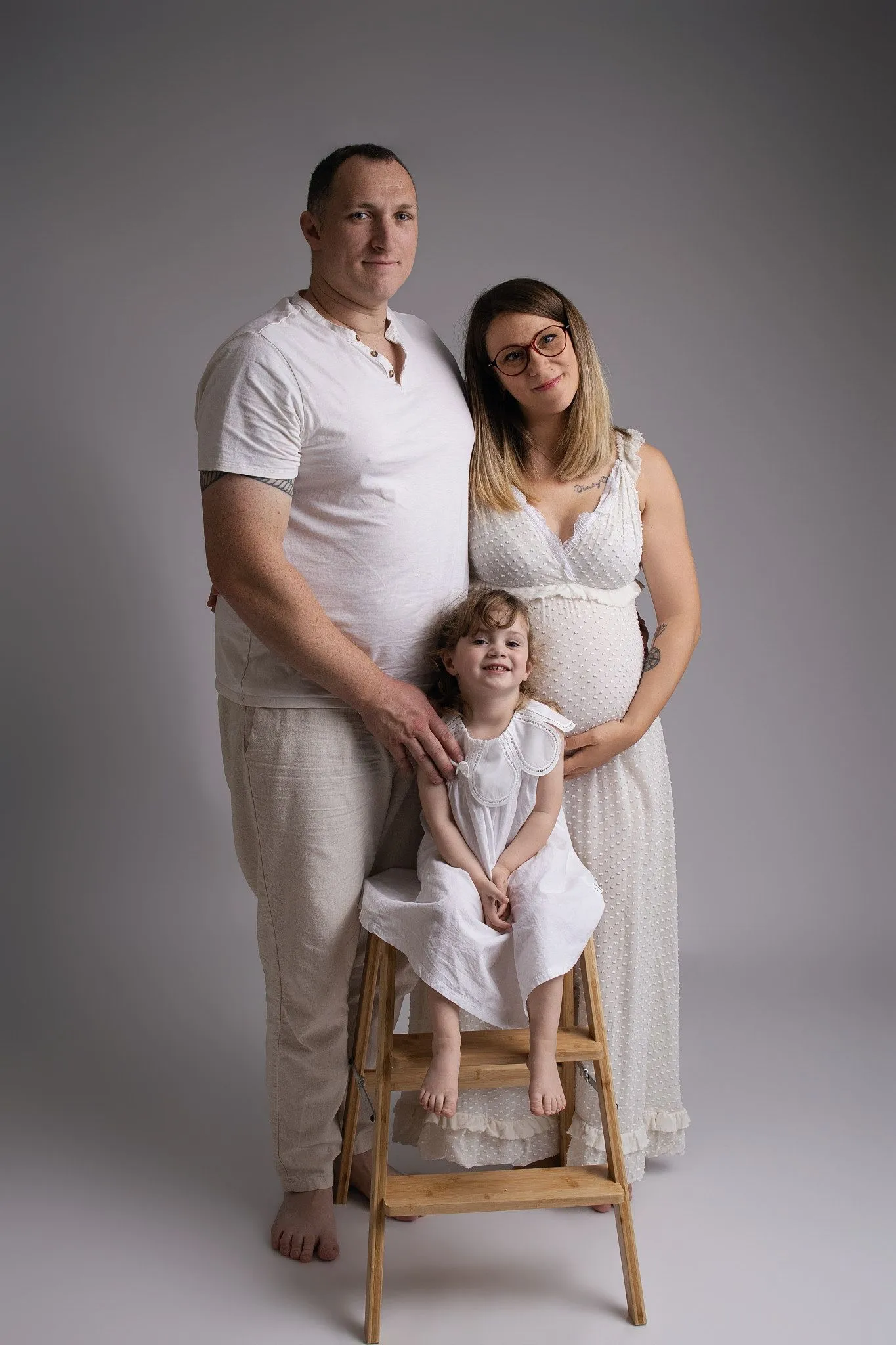 Famille en blanc avec la maman enceinte et sa fille sur un tabouret, séance maternité en studio - Cindy Poulet photographe