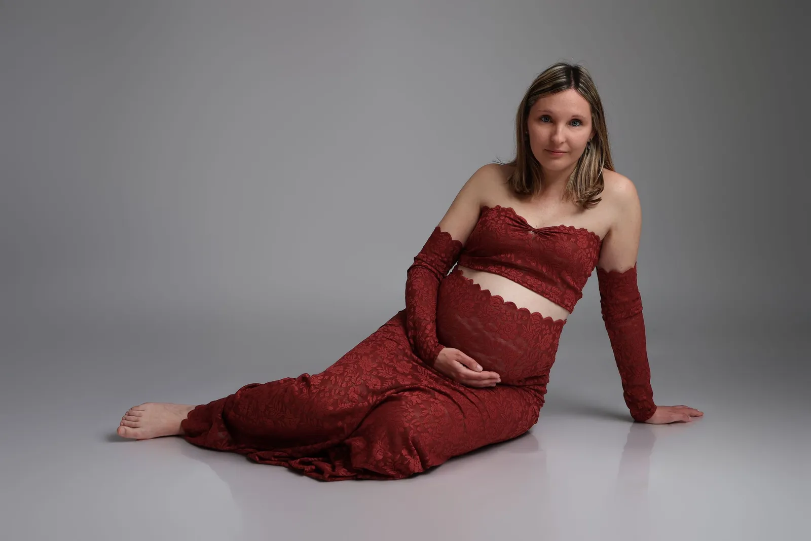 Femme enceinte en tenue rouge allongée gracieusement, séance photo grossesse - Cindy Poulet photographe