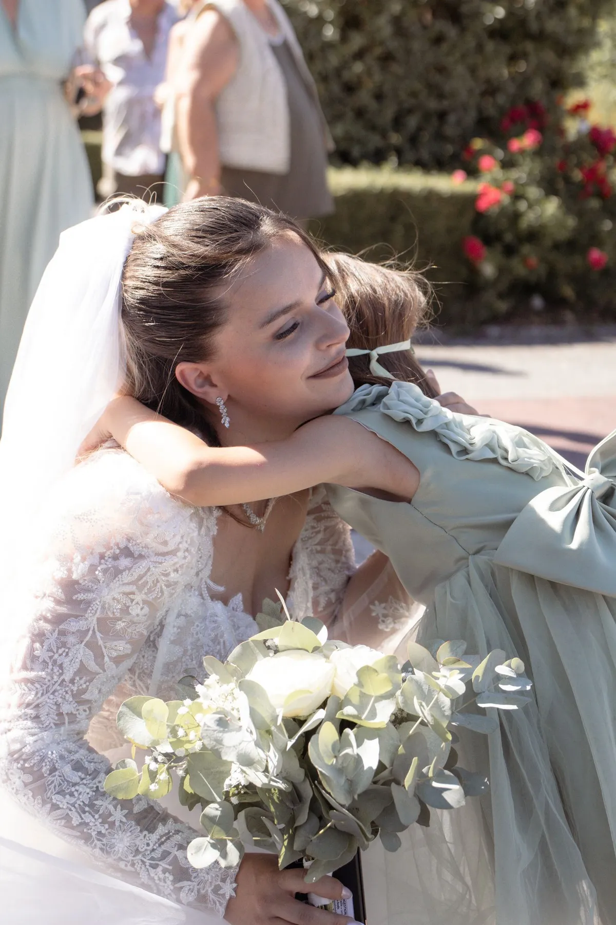 Mariée enlaçant une demoiselle d'honneur en robe vert sauge, bouquet à la main - Cindy Poulet photographe