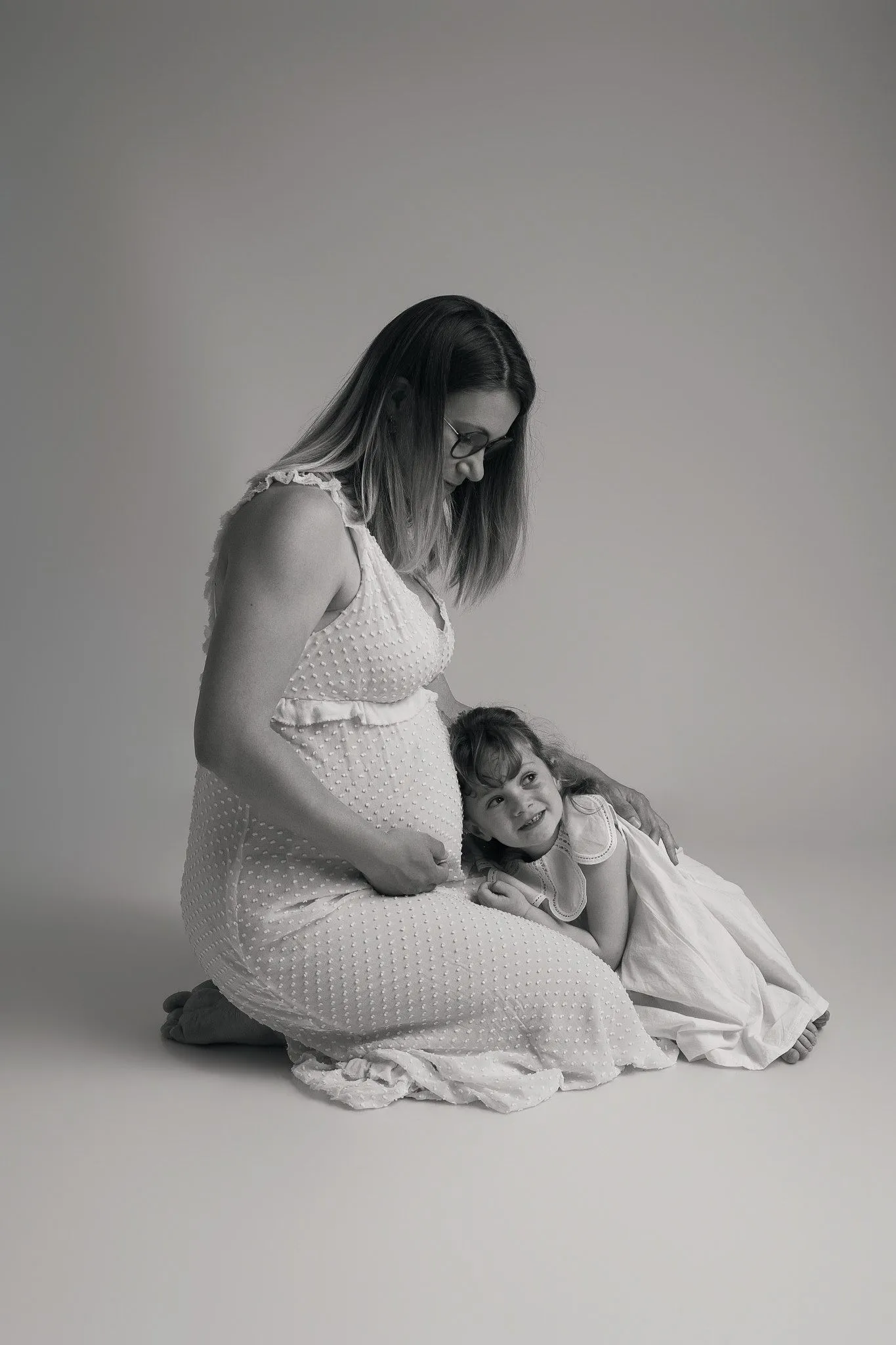 Petite fille embrassant le ventre de sa maman enceinte en studio, shooting photo maternité et famille par Cindy Poulet Photographe