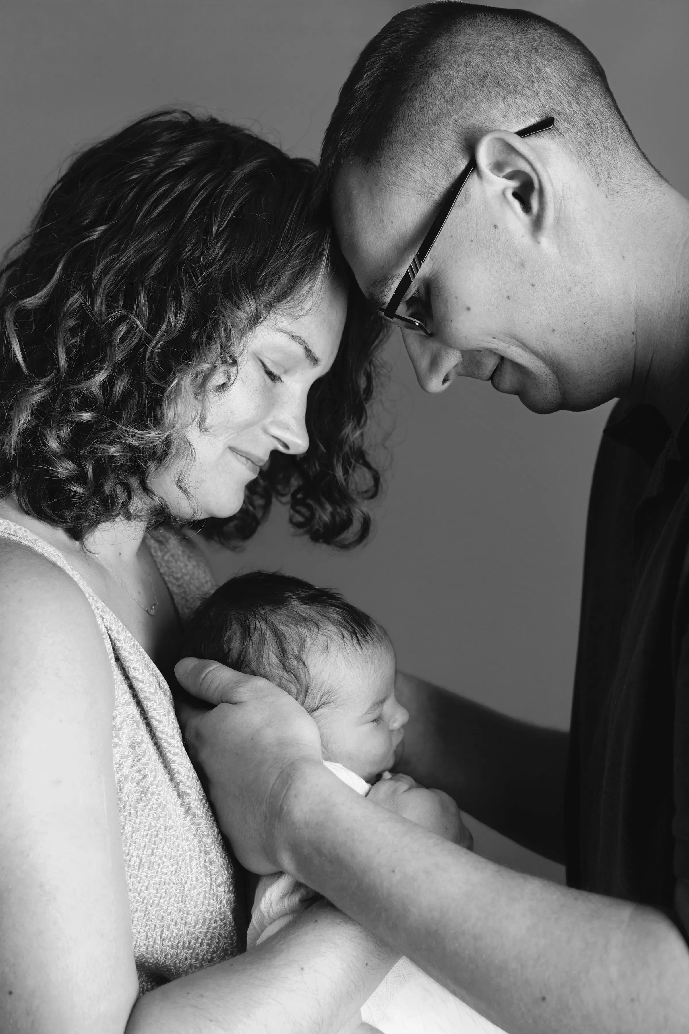 Jeunes parents blottis autour de leur nouveau-né, portrait de naissance en noir et blanc - Cindy Poulet photographe