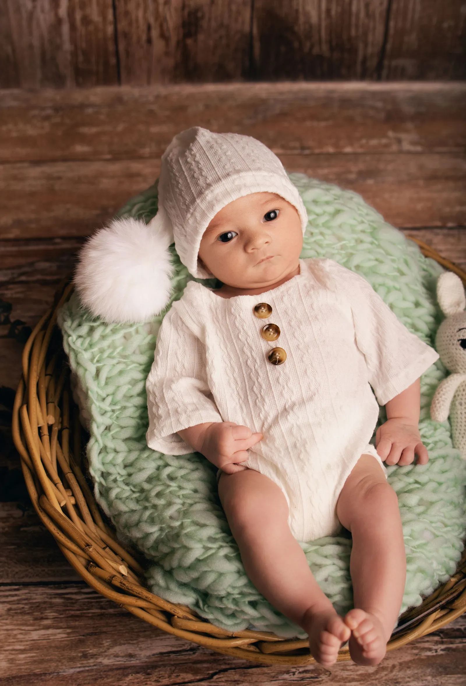 Photographie de nouveau-né par Cindy Poulet Photographe : bébé vêtu d'une tenue tricotée blanche avec bonnet à pompon.