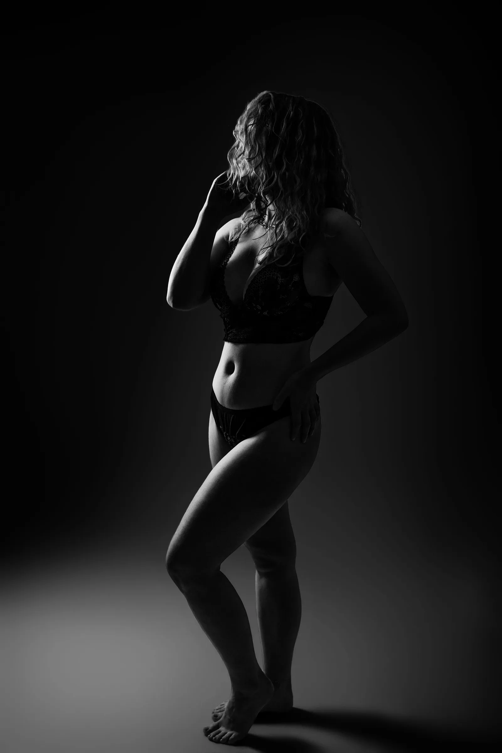 Femme en lingerie noire debout de profil dans l'obscurité, portrait boudoir sombre - Cindy Poulet photographe