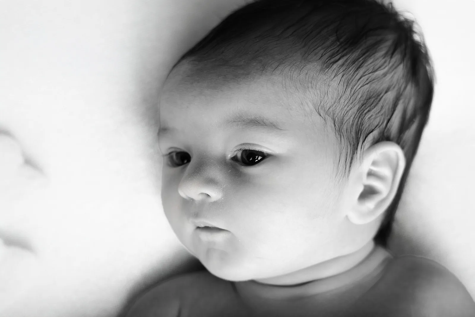 Portrait de naissance en noir et blanc par Cindy Poulet Photographe : gros plan artistique sur le visage d'un nouveau-né au regard calme et