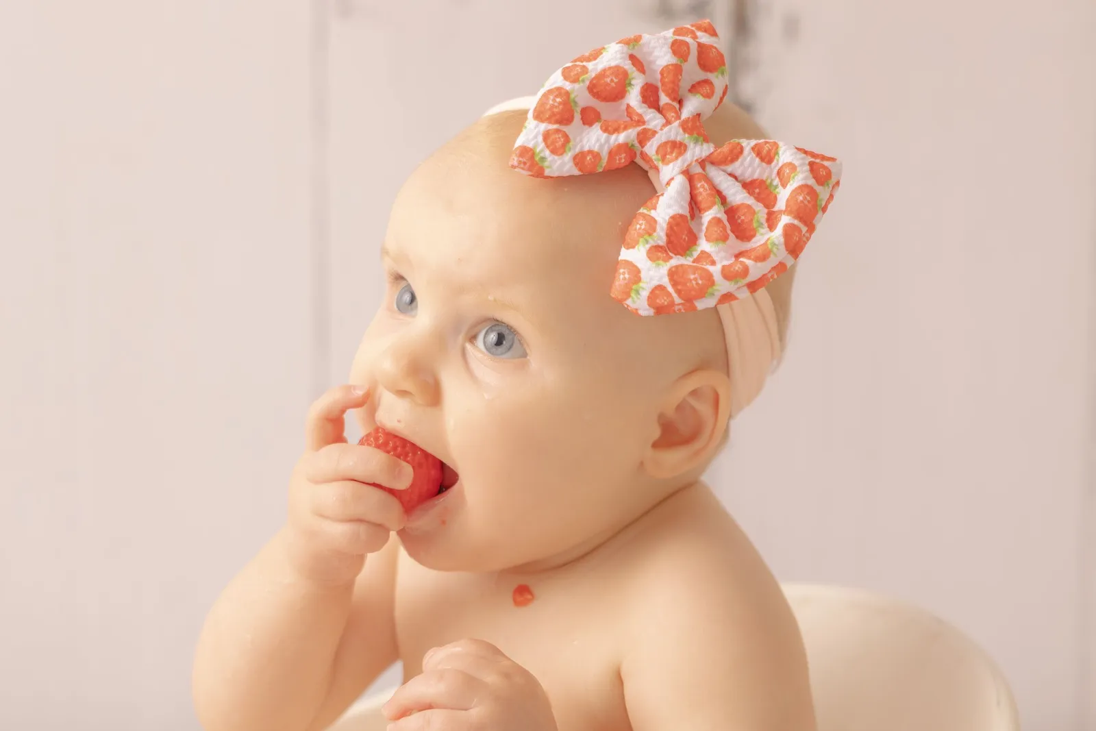 Séance photo bébé thématique par Cindy Poulet Photographe : portrait d'un enfant avec un bandeau à nœud fraise croquant une fraise.