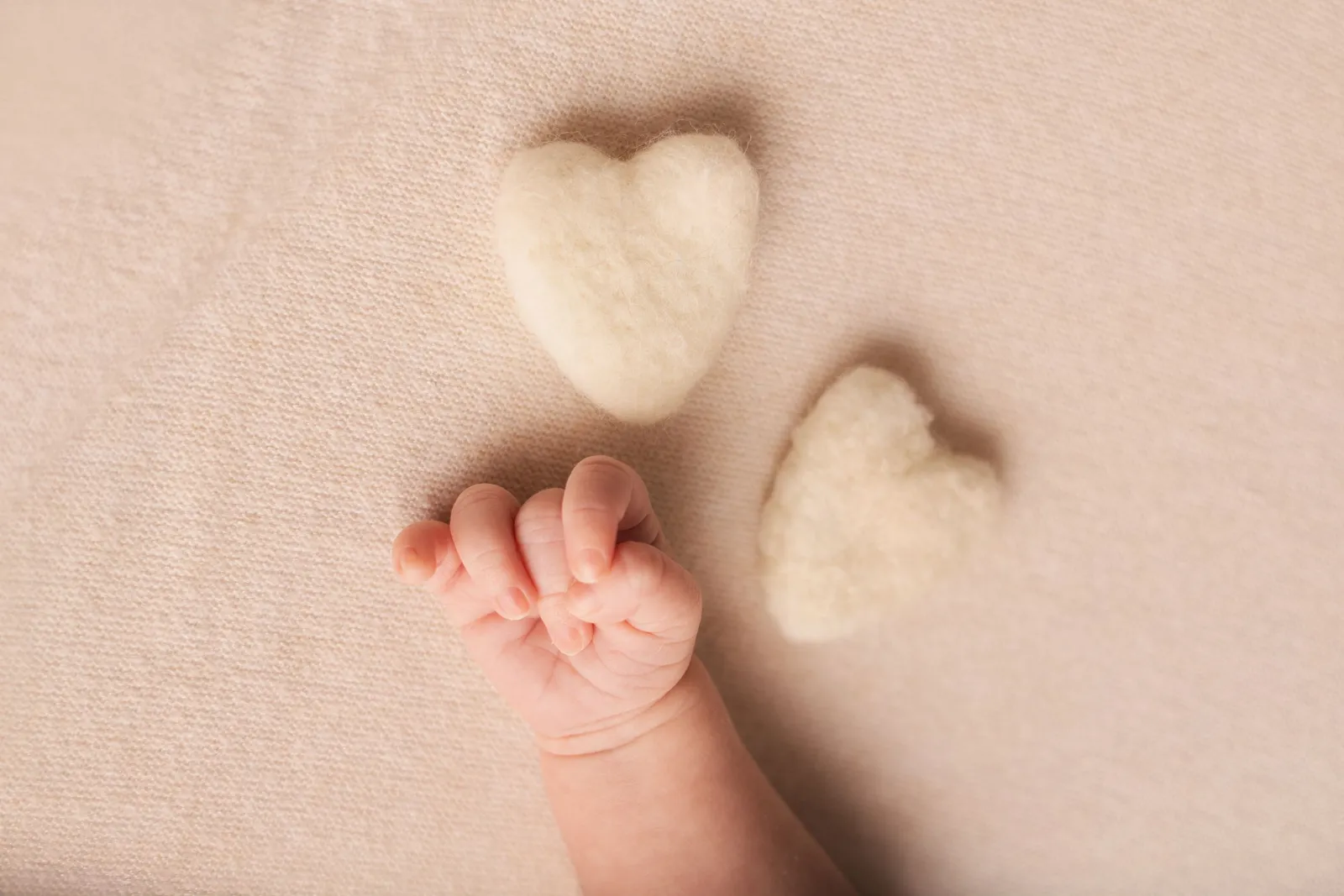 Détail de séance photo nouveau-né par Cindy Poulet Photographe : gros plan sur la main d'un bébé à côté de deux petits cœurs en laine.