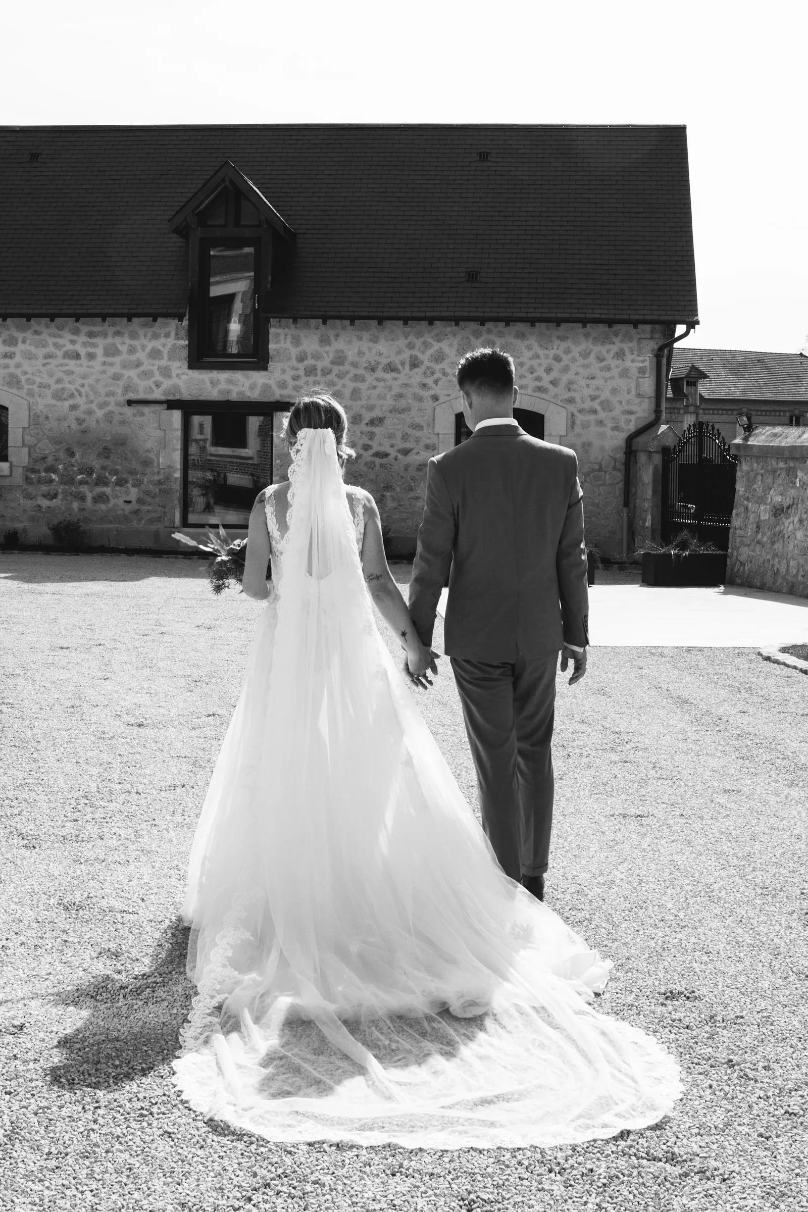 Mariée en robe blanche marchant main dans la main avec le marié, photo de mariage noir et blanc - Cindy Poulet photographe