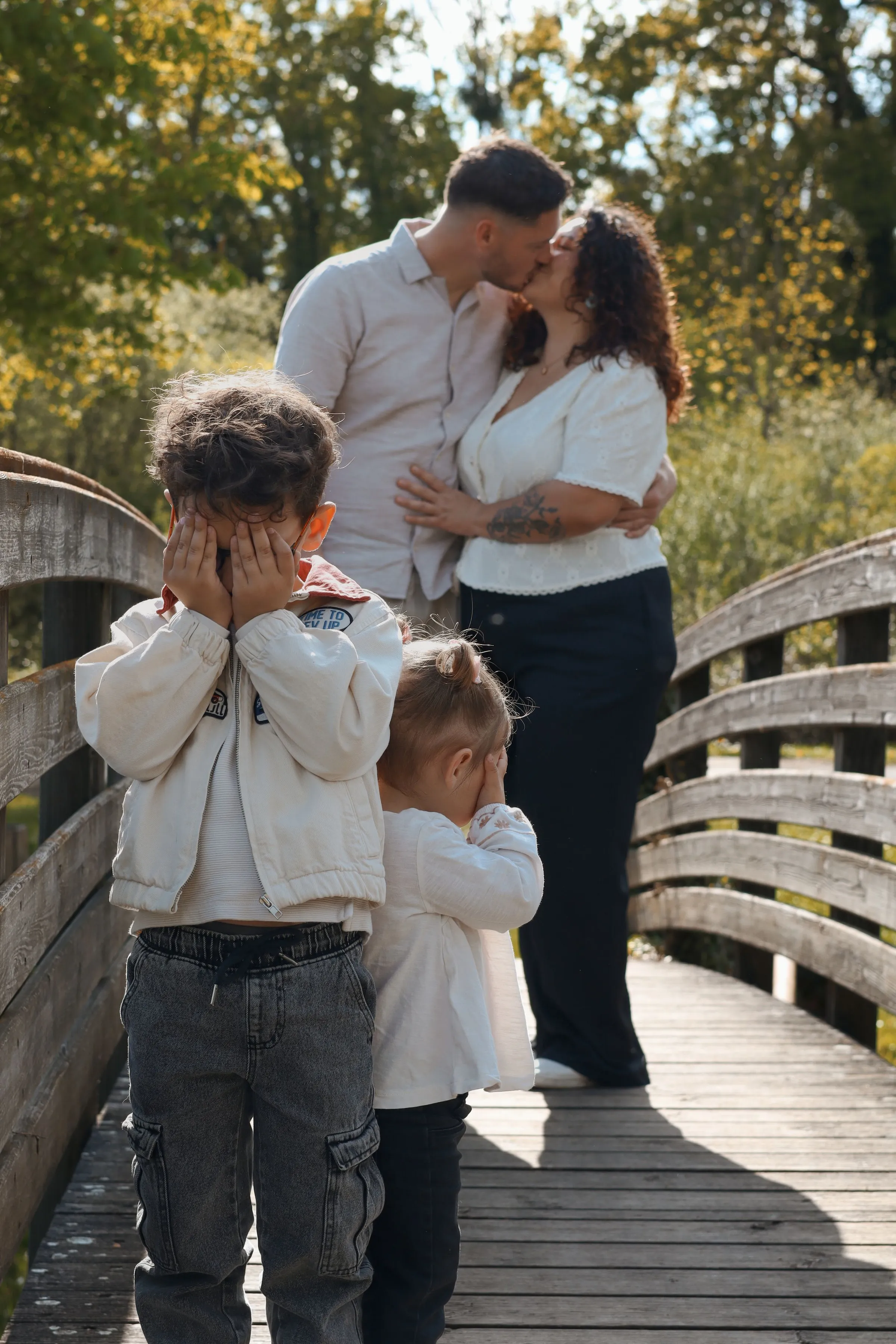 Famille avec parents s'embrassant sur un pont en bois et enfants devant, photo en extérieur - Cindy Poulet photographe