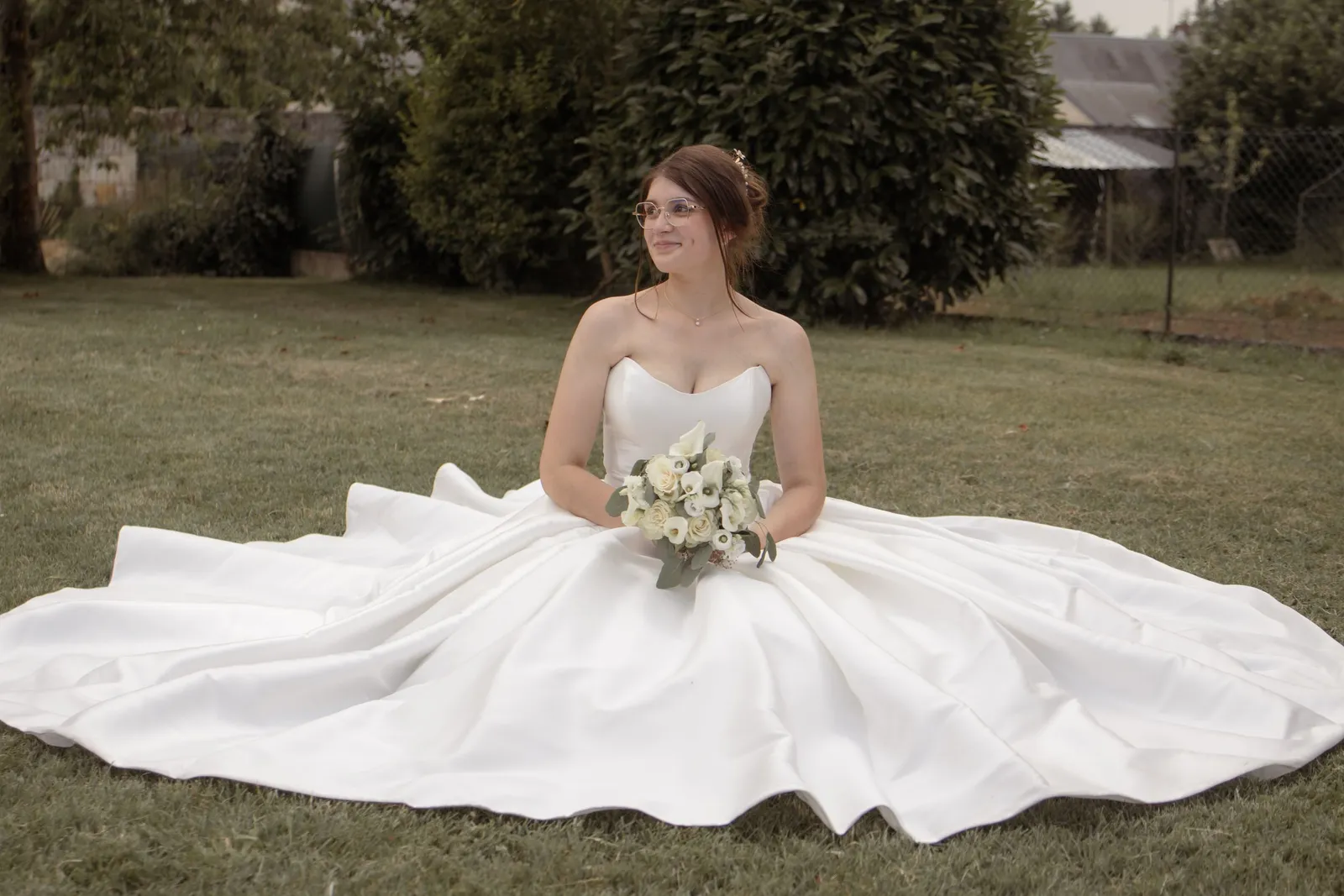 Mariée assise dans l'herbe, robe déployée et bouquet sur les genoux - Cindy Poulet photographe