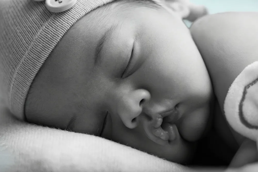 Gros plan en noir et blanc d'un nouveau-né endormi avec son bonnet - Cindy Poulet photographe
