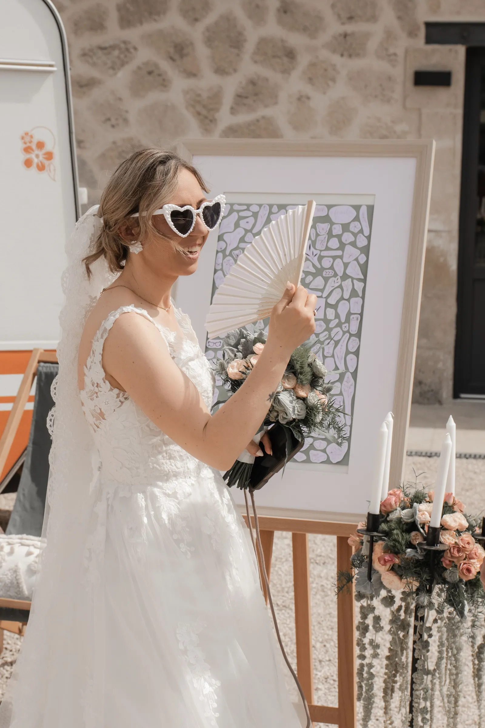 Mariée avec éventail et lunettes de soleil coeur devant tableau de mariage - Cindy Poulet photographe