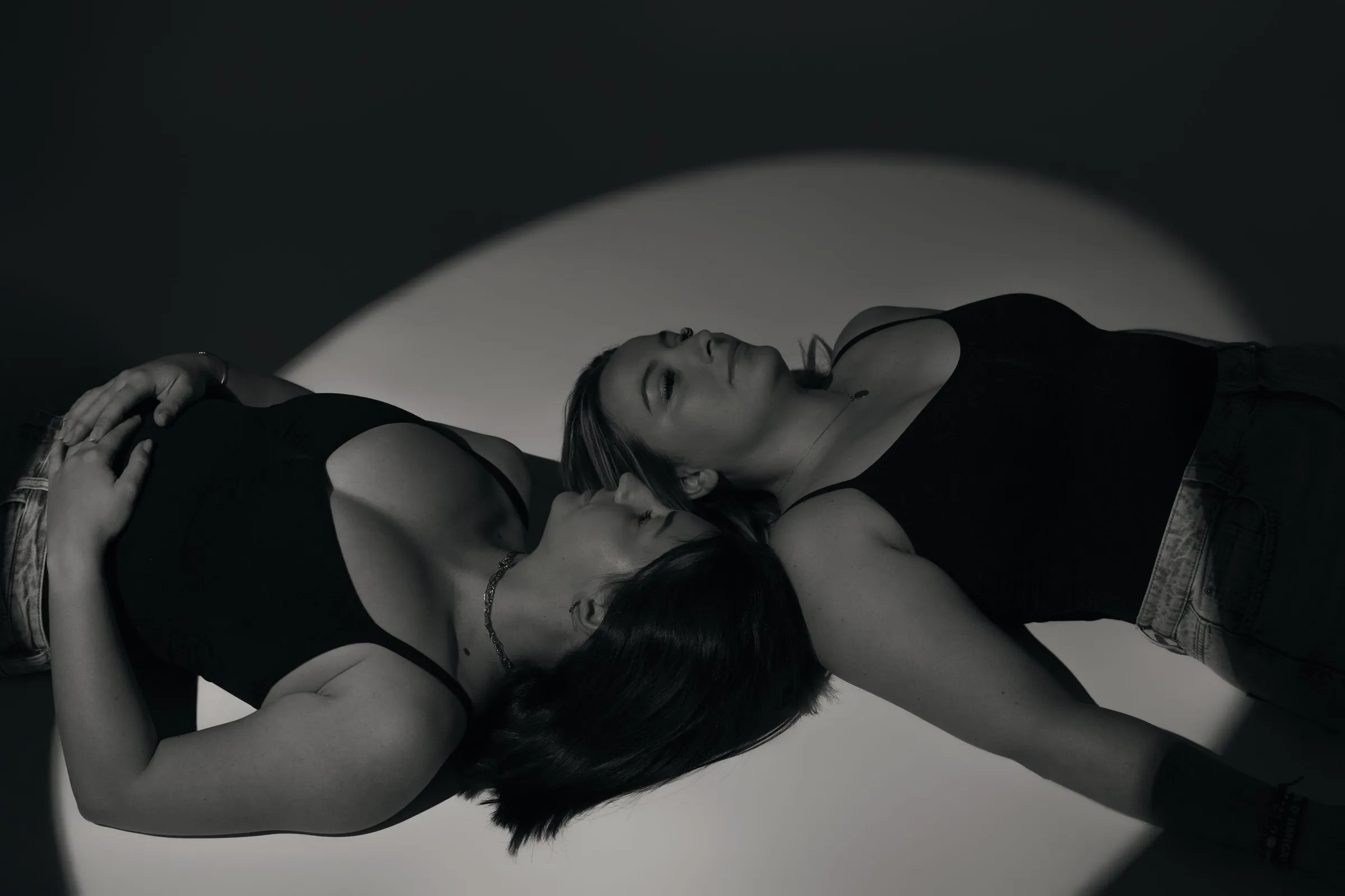 Deux femmes allongées tête contre tête dans un cercle de lumière, portrait artistique en noir et blanc - Cindy Poulet photographe
