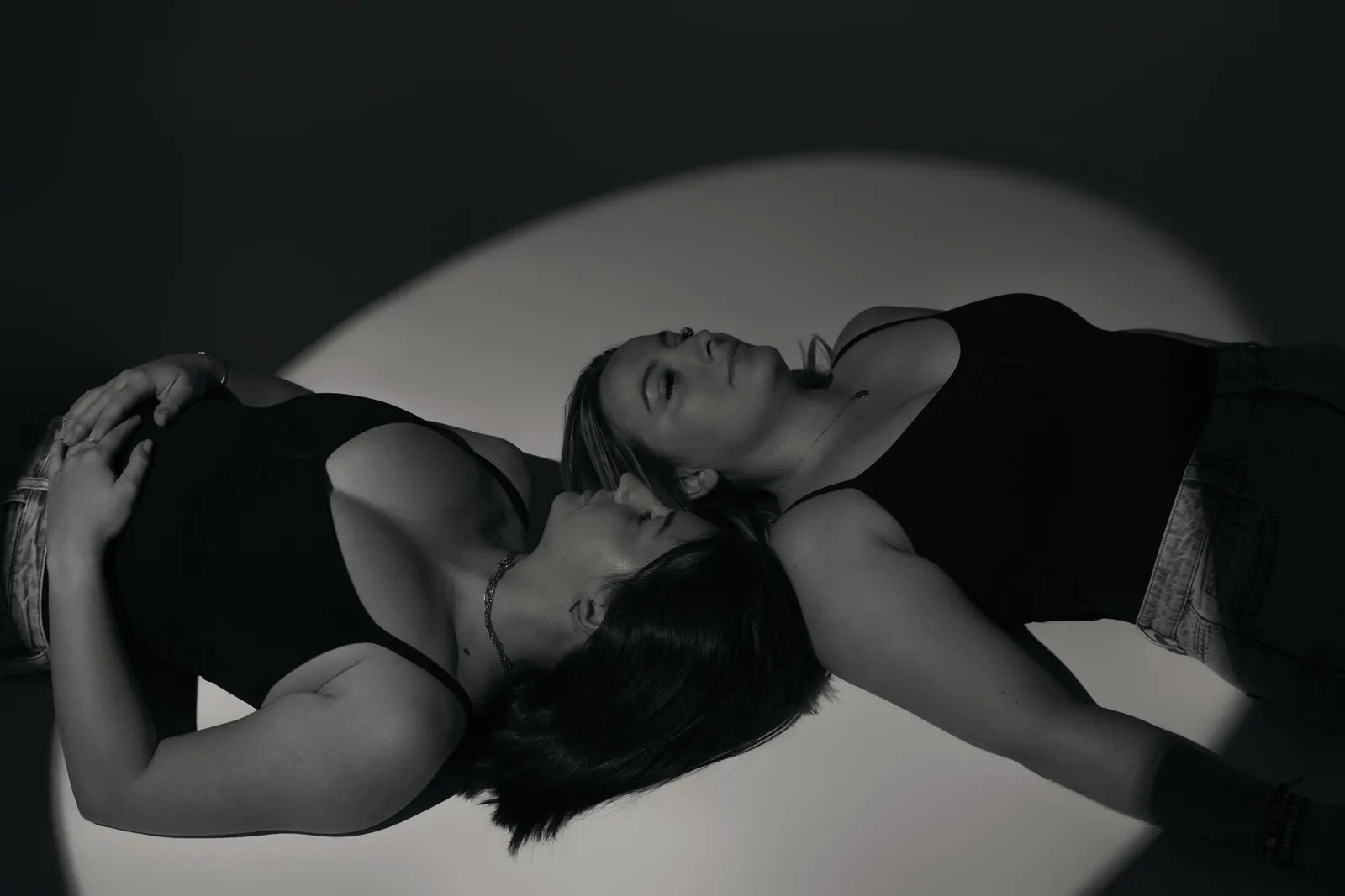 Deux femmes allongées tête contre tête dans un cercle de lumière, portrait artistique en noir et blanc - Cindy Poulet photographe