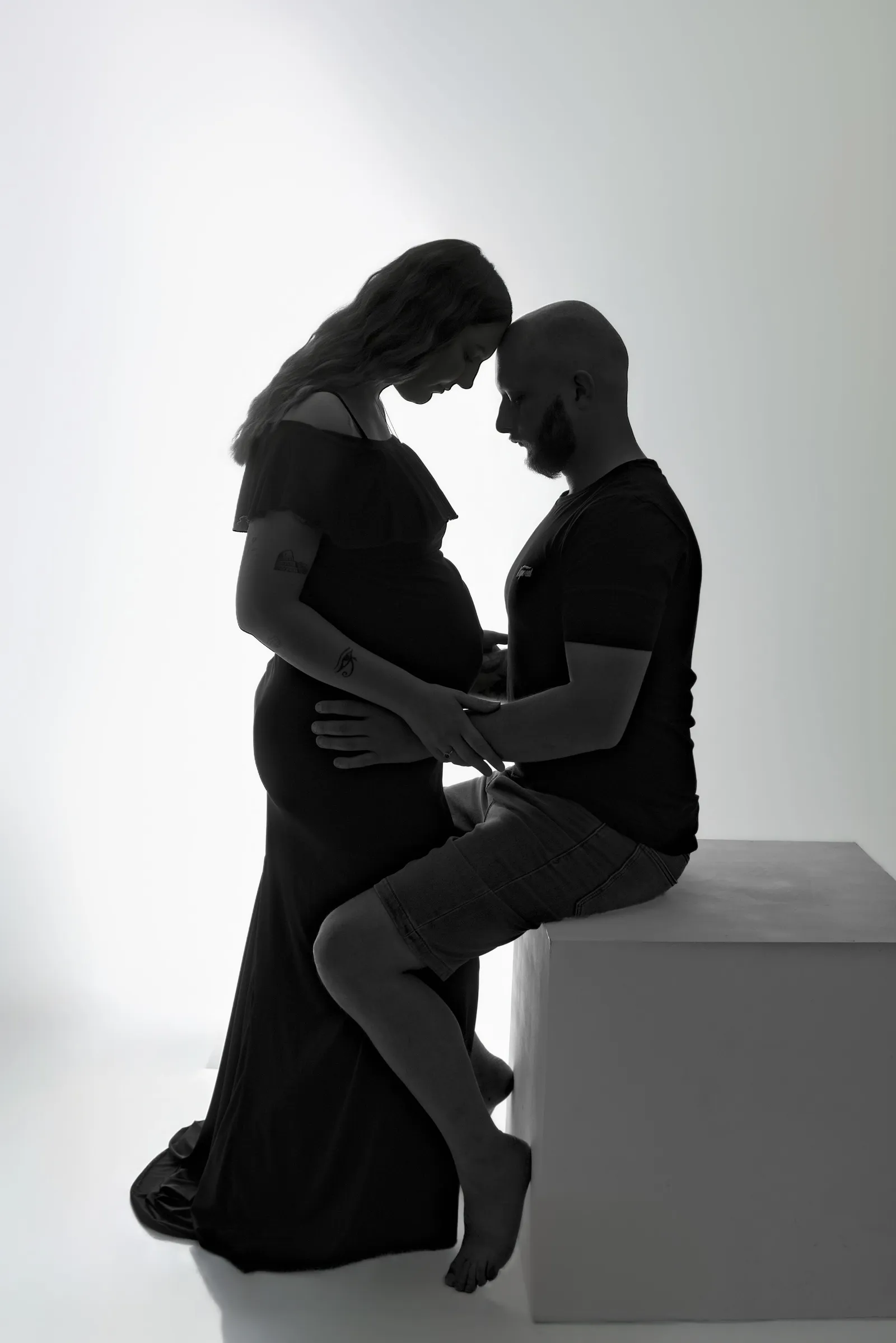 Silhouette en noir et blanc de couple enceinte assis face à face, portrait maternité artistique - Cindy Poulet photographe