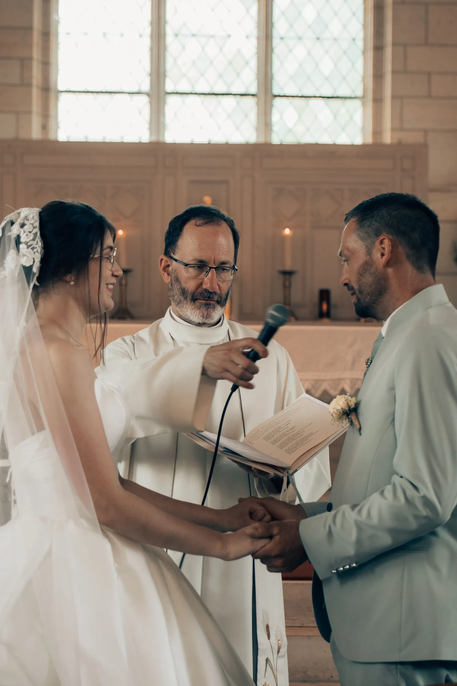 Cérémonie religieuse à l'église, les mariés main dans la main face au célébrant - Cindy Poulet photographe