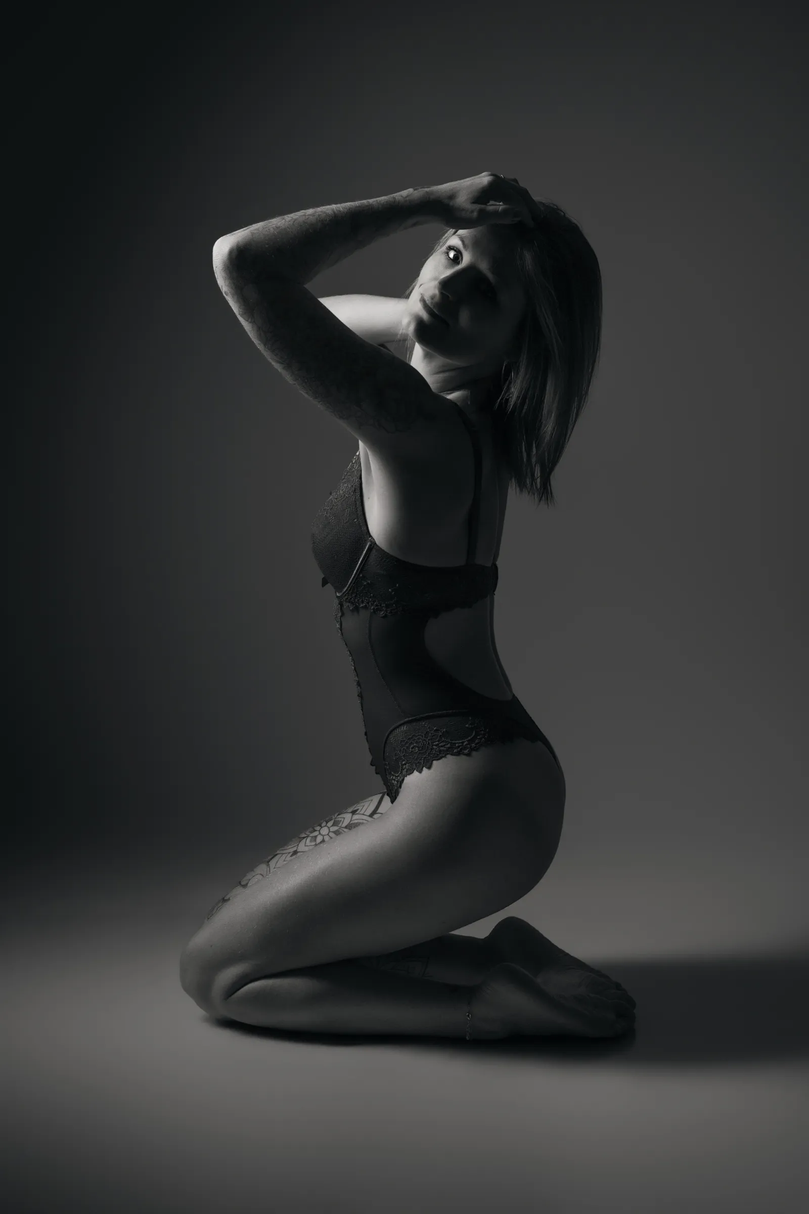 Femme en body noir à genoux, une main dans les cheveux, dans un clair-obscur de studio, portrait boudoir - Cindy Poulet photographe