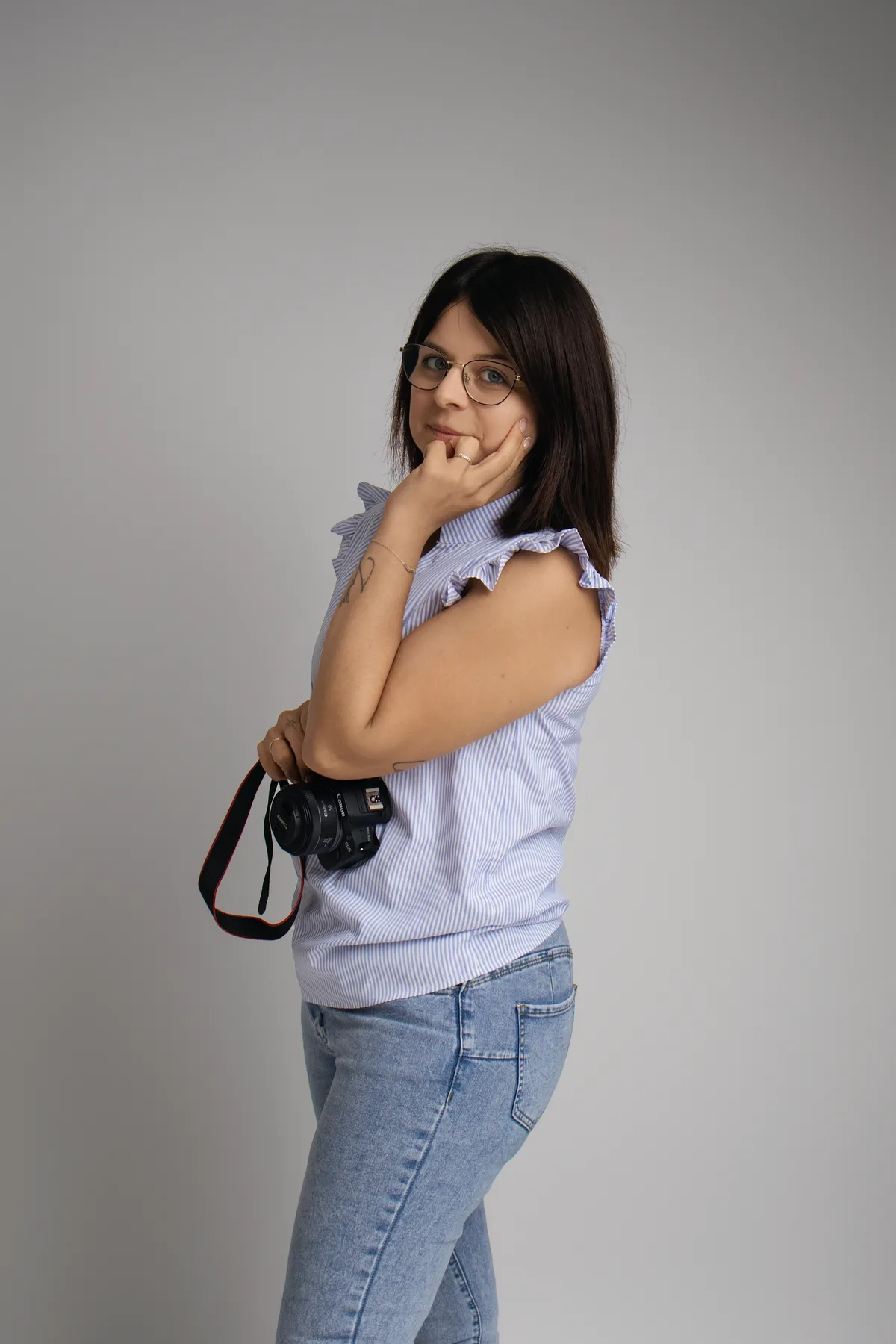 Cindy Poulet debout dans son studio de Septvaux, son appareil photo à la main, souriante en chemise rayée.