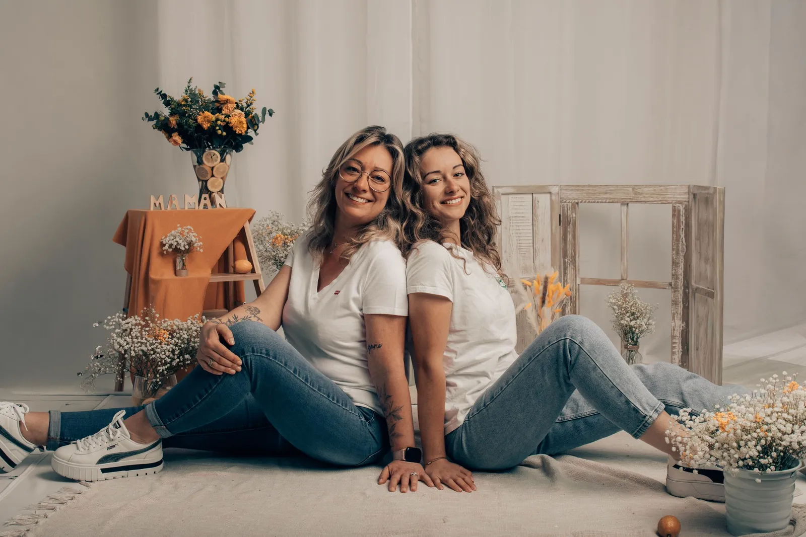Deux femmes assises par terre en jeans blancs entourées de fleurs, portrait duo - Cindy Poulet photographe