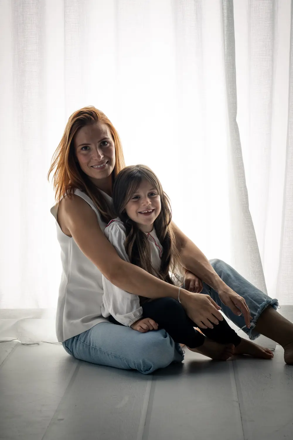 Une maman et sa fille blotties assises au sol devant des voilages blancs, séance famille en studio à Septvaux - Cindy Poulet photographe