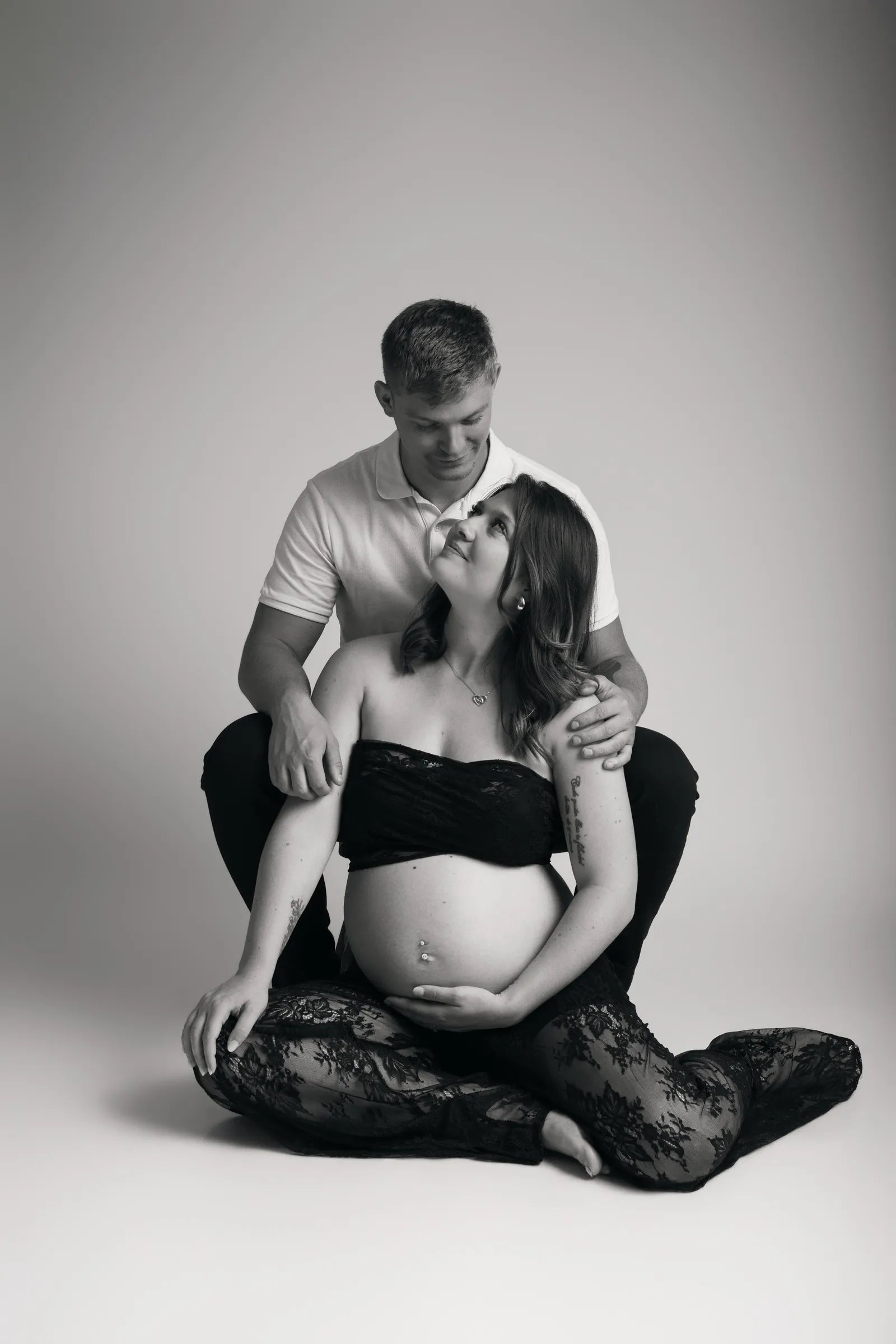 Couple assis au sol en studio, la future maman adossée à son compagnon, portrait de grossesse en noir et blanc - Cindy Poulet photographe