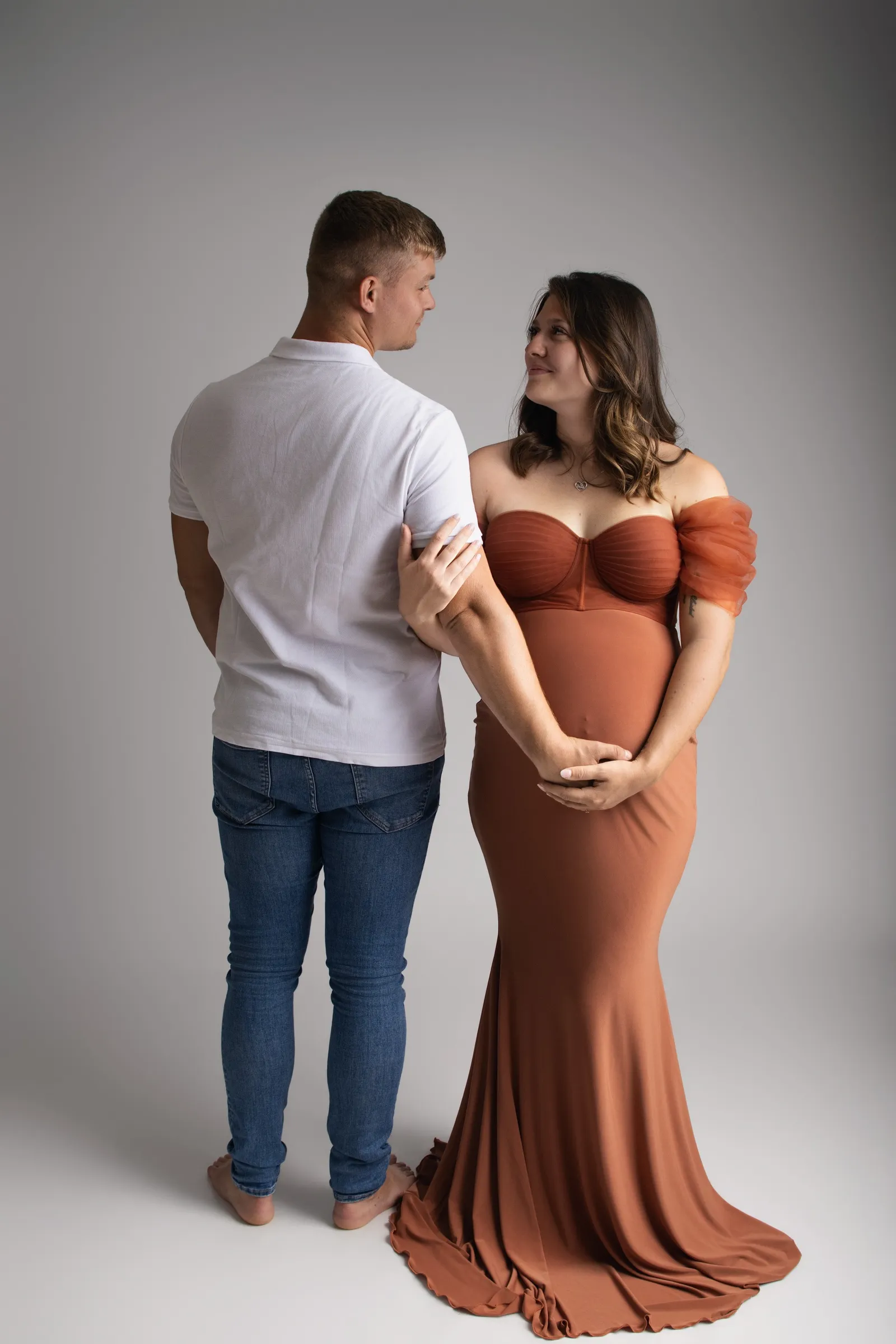 Future maman en robe terracotta regardant son compagnon de dos, portrait de couple en studio - Cindy Poulet photographe