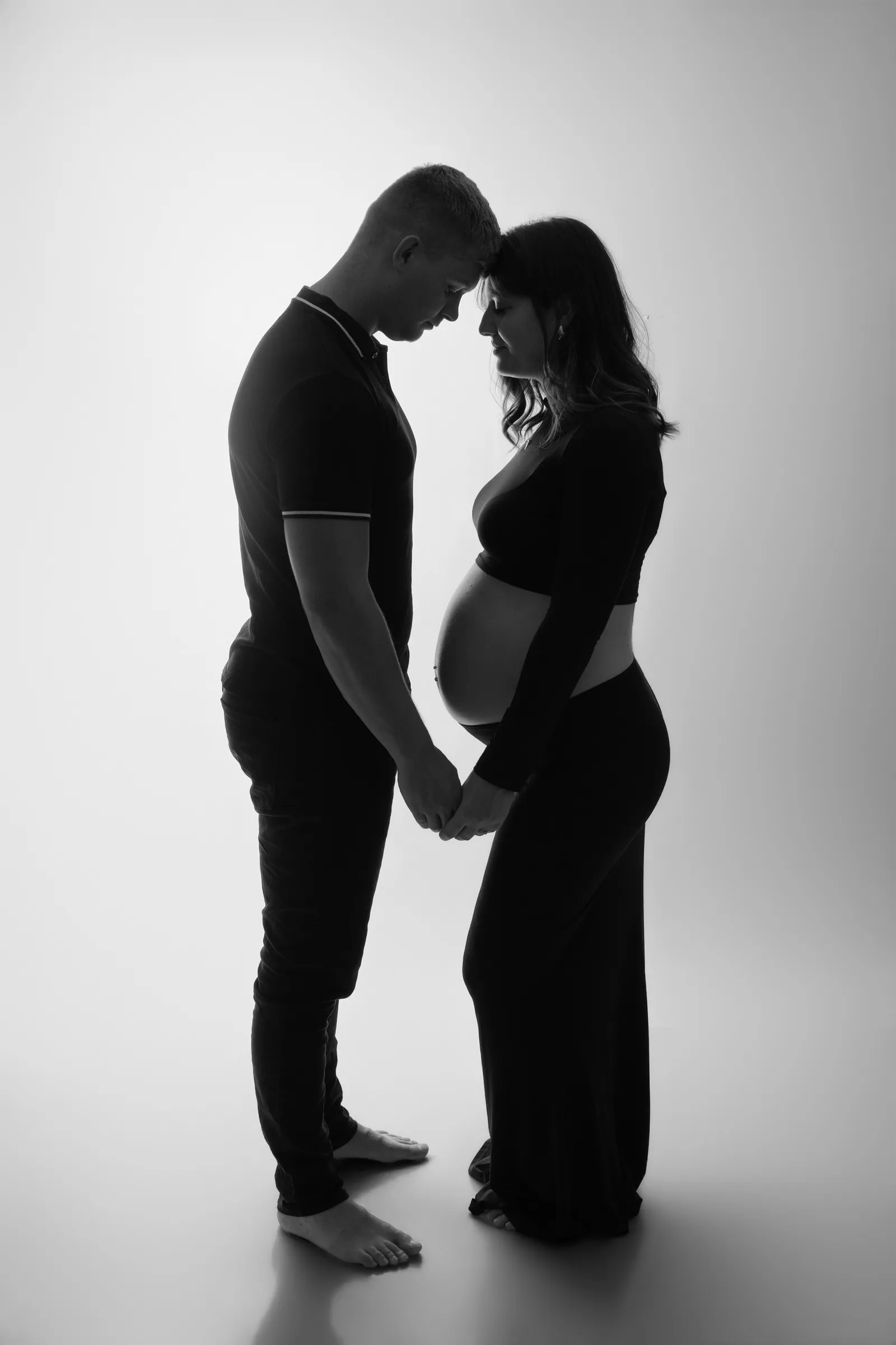 Futurs parents front contre front main dans la main, silhouette de grossesse en noir et blanc - Cindy Poulet photographe