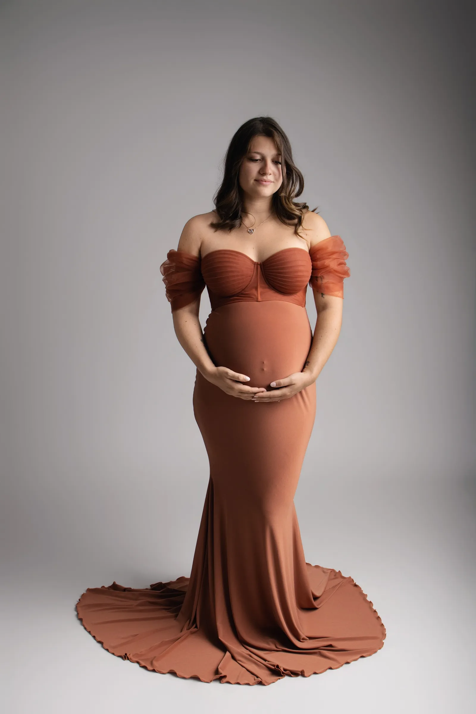 Femme enceinte de face en robe longue terracotta à traîne, mains sur son ventre rond en studio - Cindy Poulet photographe