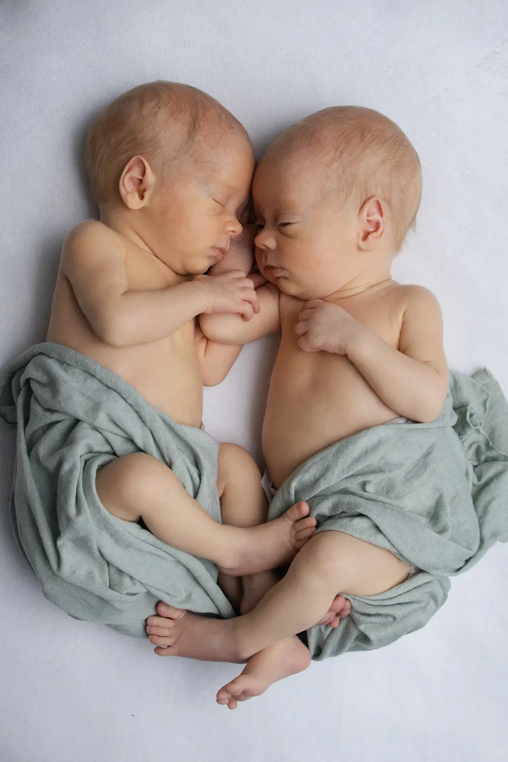 Jumeaux nouveau-nés endormis face à face, enveloppés dans un lange vert d'eau, séance photo naissance - Cindy Poulet photographe