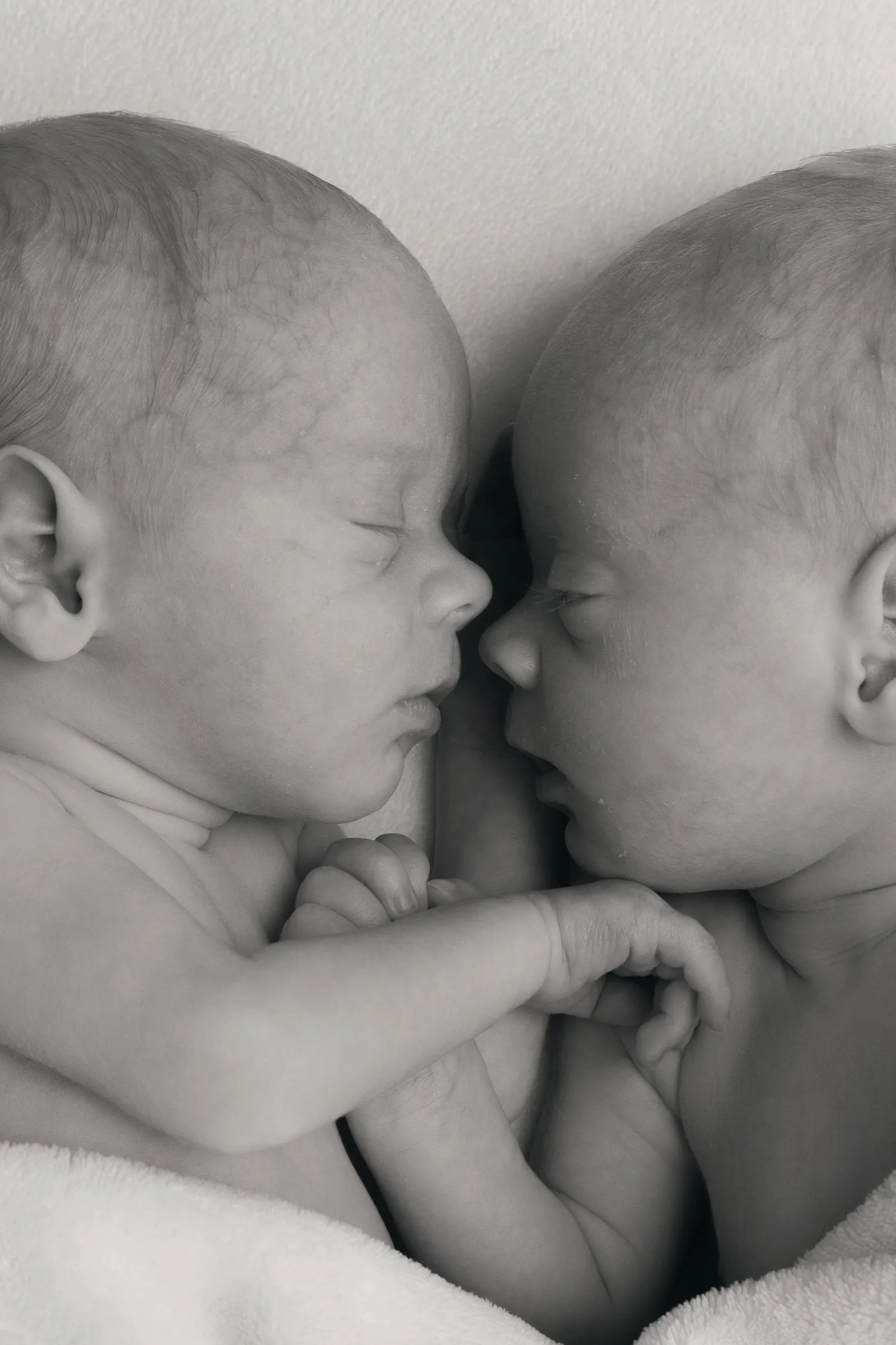 Gros plan en noir et blanc sur des jumeaux nouveau-nés endormis face à face, portrait naissance - Cindy Poulet photographe