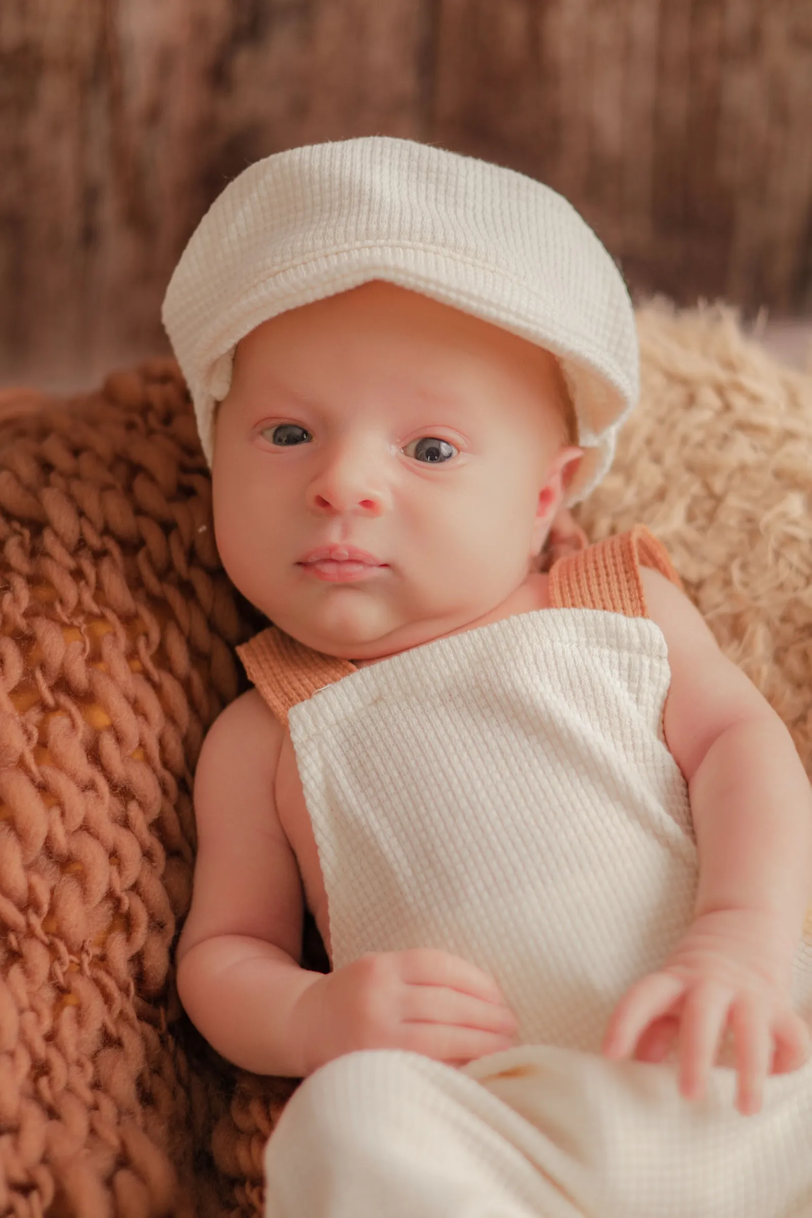 Portrait de nouveau-né par Cindy Poulet Photographe : bébé portant une petite casquette et une salopette blanche.