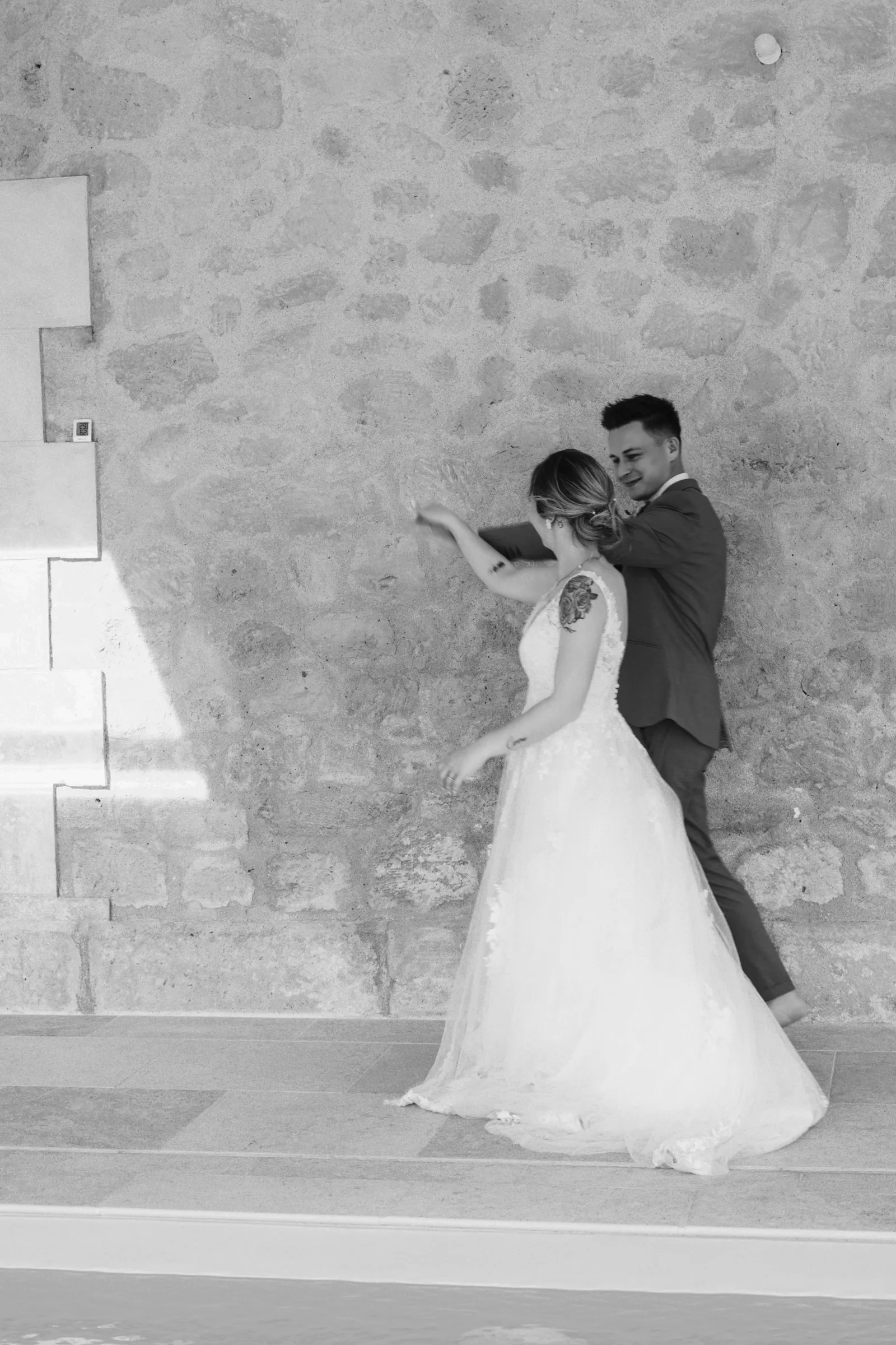 Couple de mariés en noir et blanc devant un mur en pierre, photo de mariage - Cindy Poulet photographe