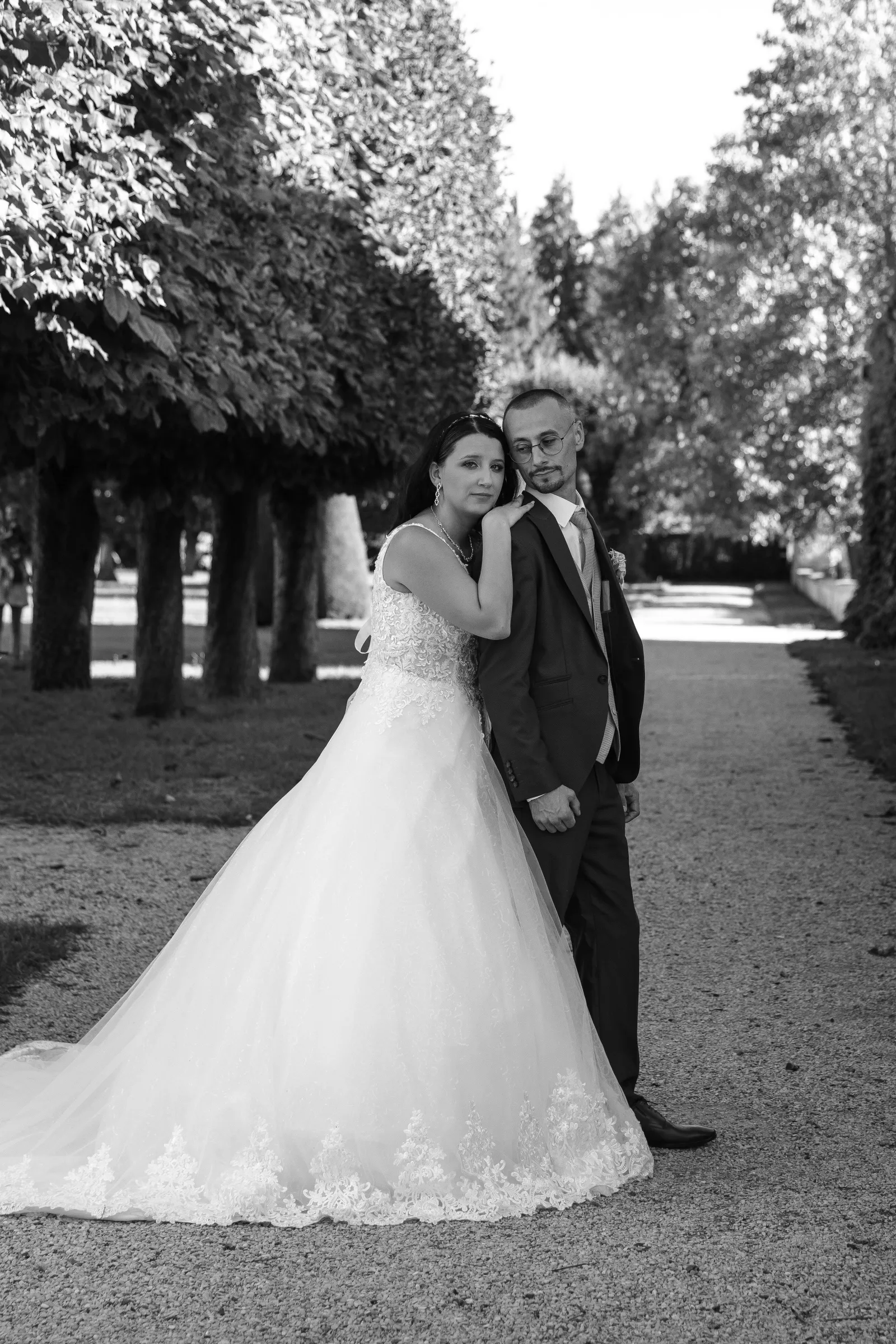 Mariés enlacés dans une allée bordée d'arbres taillés, portrait de couple en noir et blanc - Cindy Poulet photographe