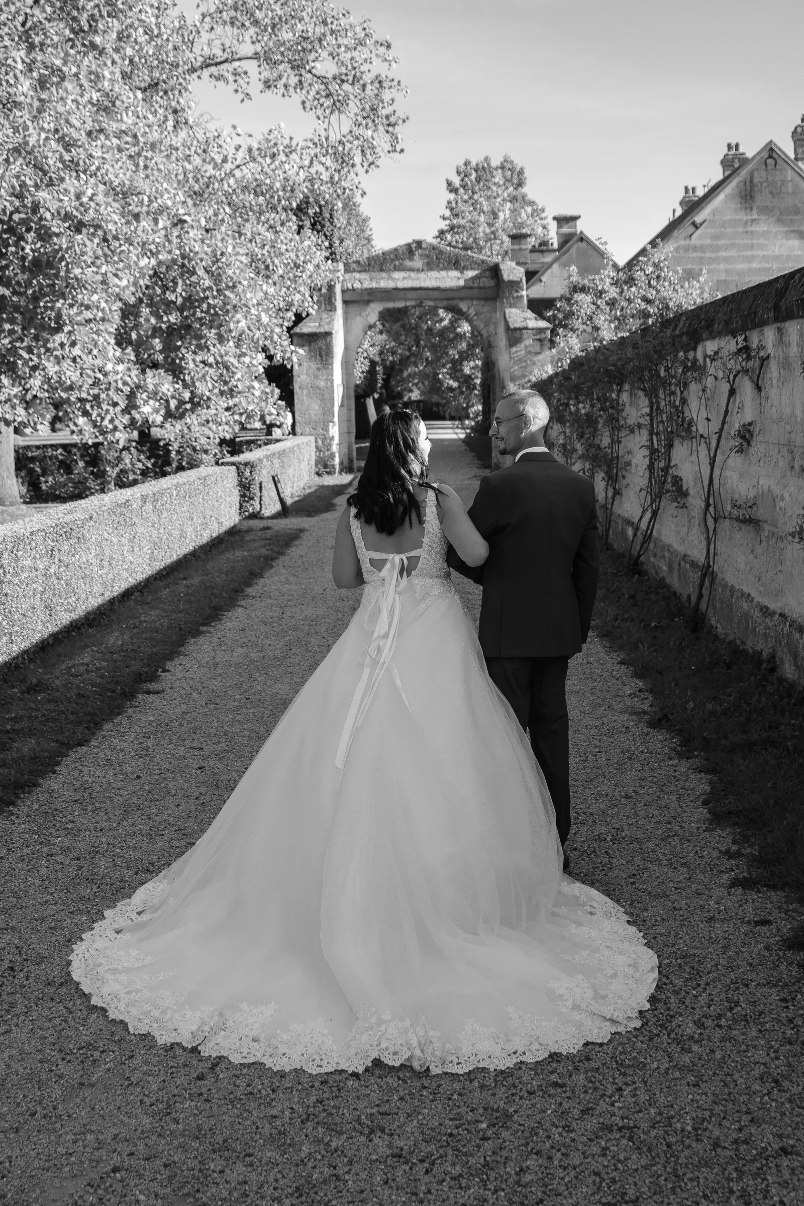 Mariée remontant l'allée au bras de son père, vue de dos en noir et blanc - Cindy Poulet photographe