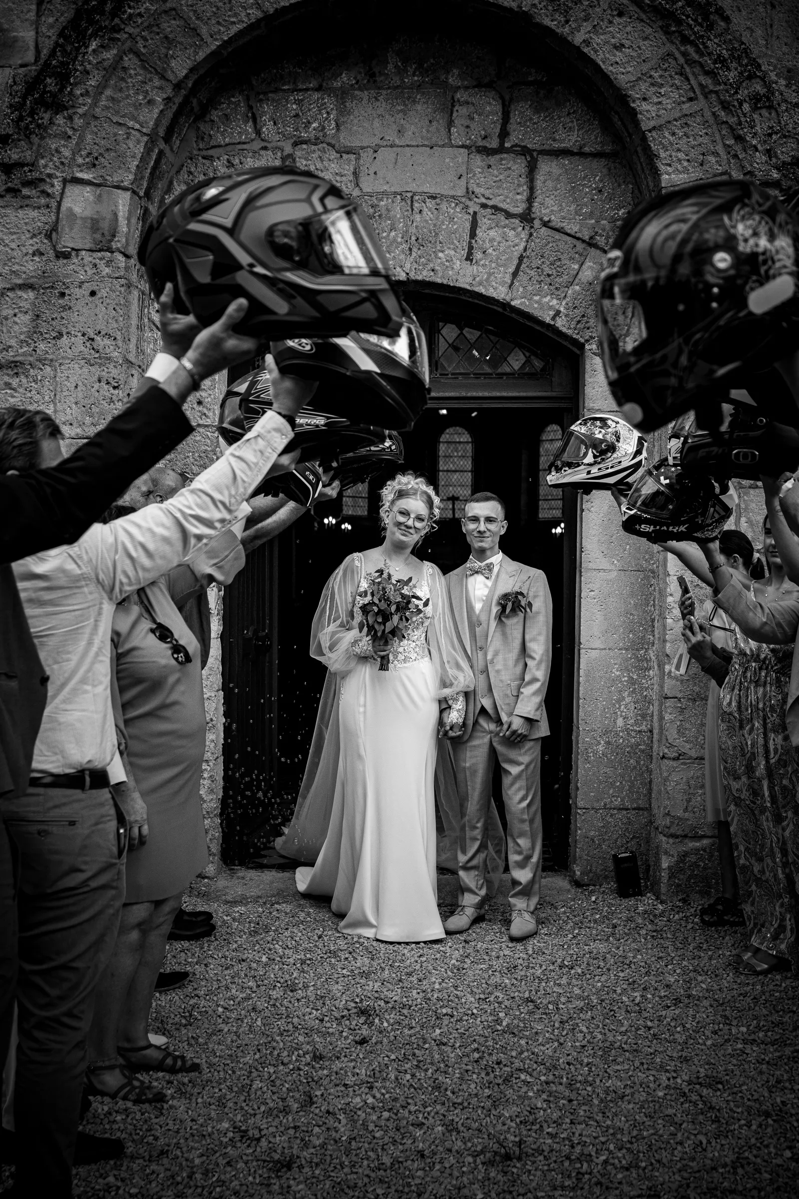 Sortie de l'église des mariés sous une haie d'honneur de casques de moto, photo de mariage en noir et blanc - Cindy Poulet photographe