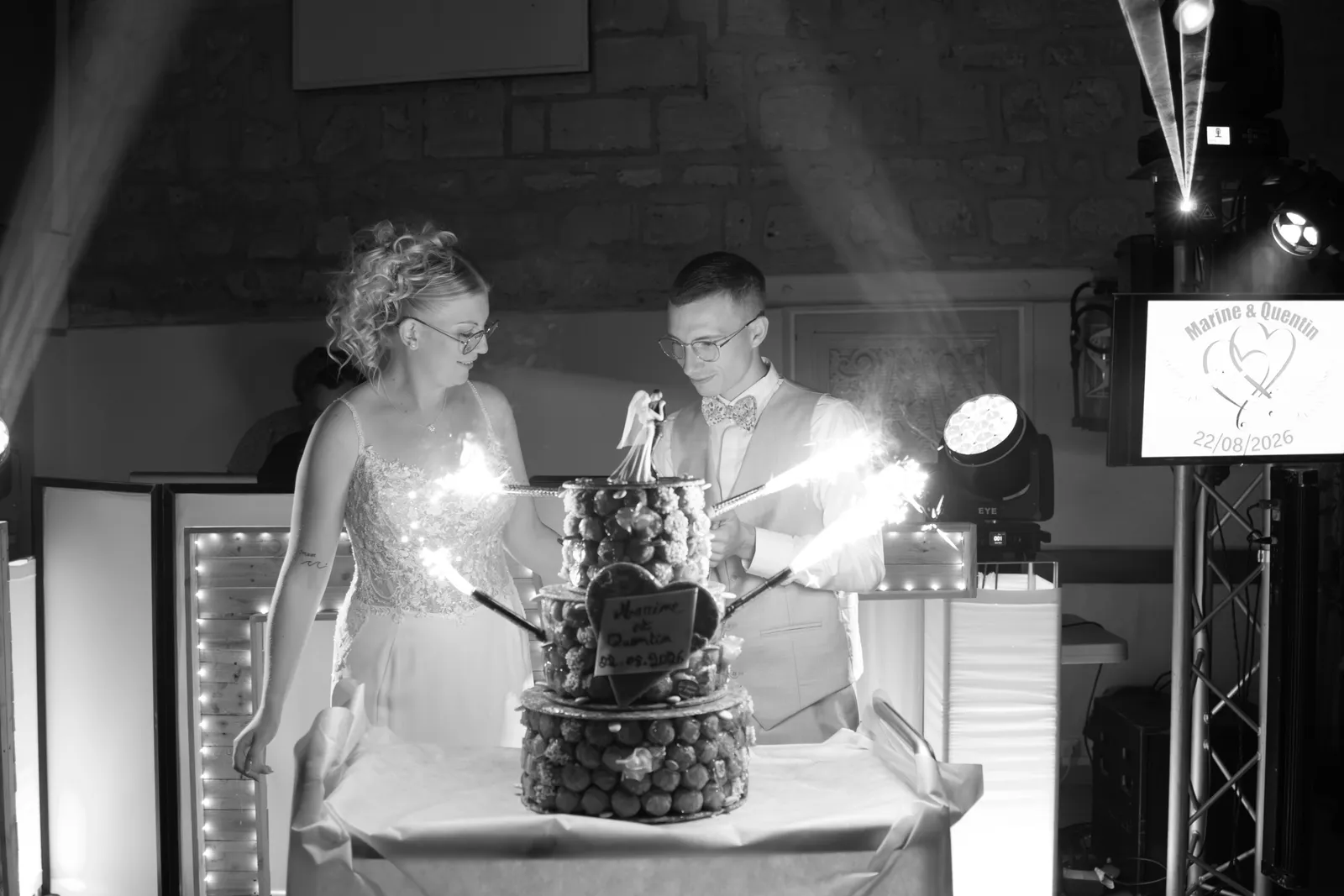 Les mariés découpant la pièce montée sous les feux de Bengale, soirée de mariage en noir et blanc - Cindy Poulet photographe