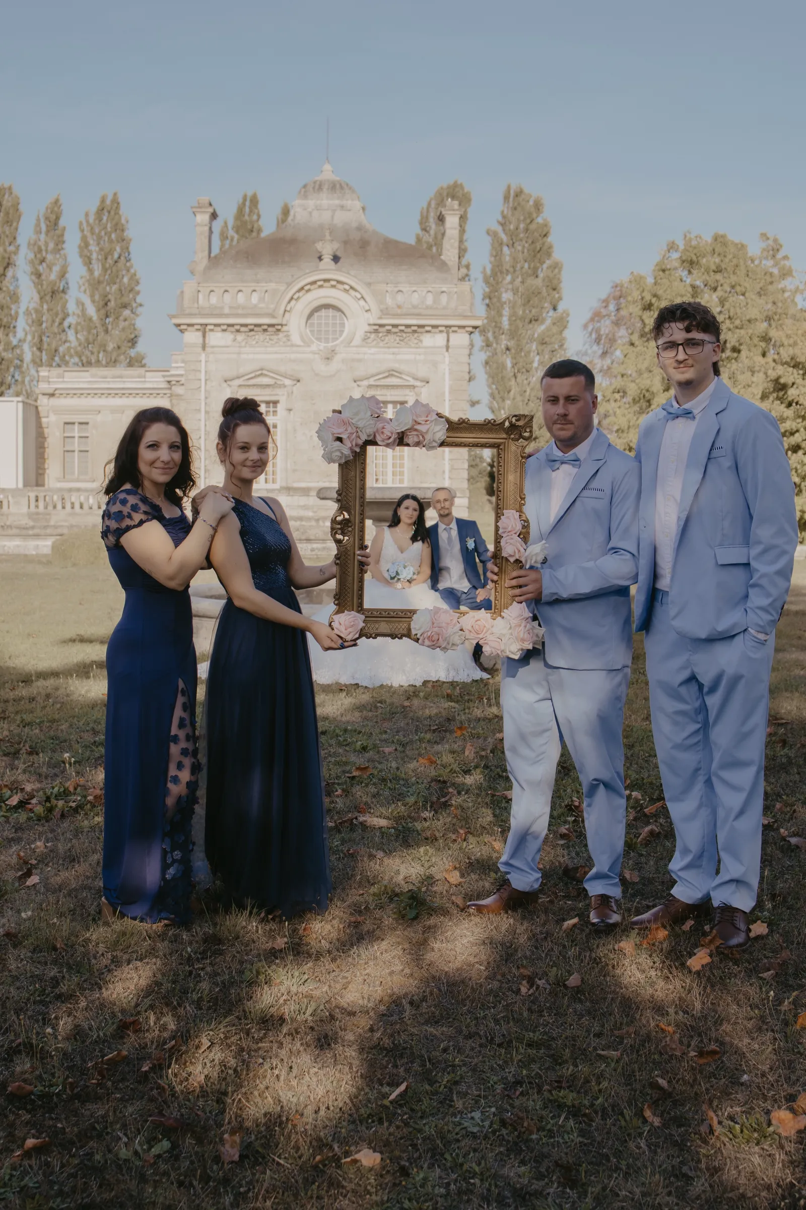 Témoins posant avec un cadre doré fleuri devant un château, photo de groupe de mariage - Cindy Poulet photographe