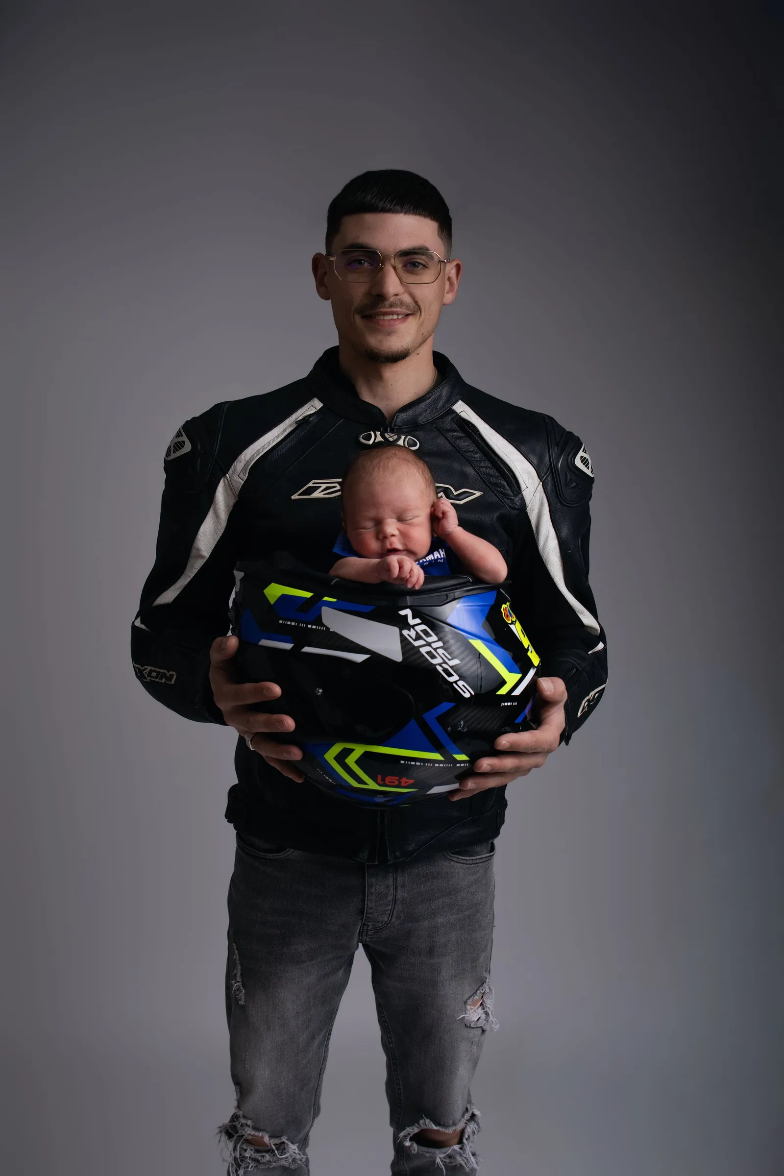 Père en veste de moto tenant son nouveau-né dans son casque, portrait naissance original - Cindy Poulet photographe