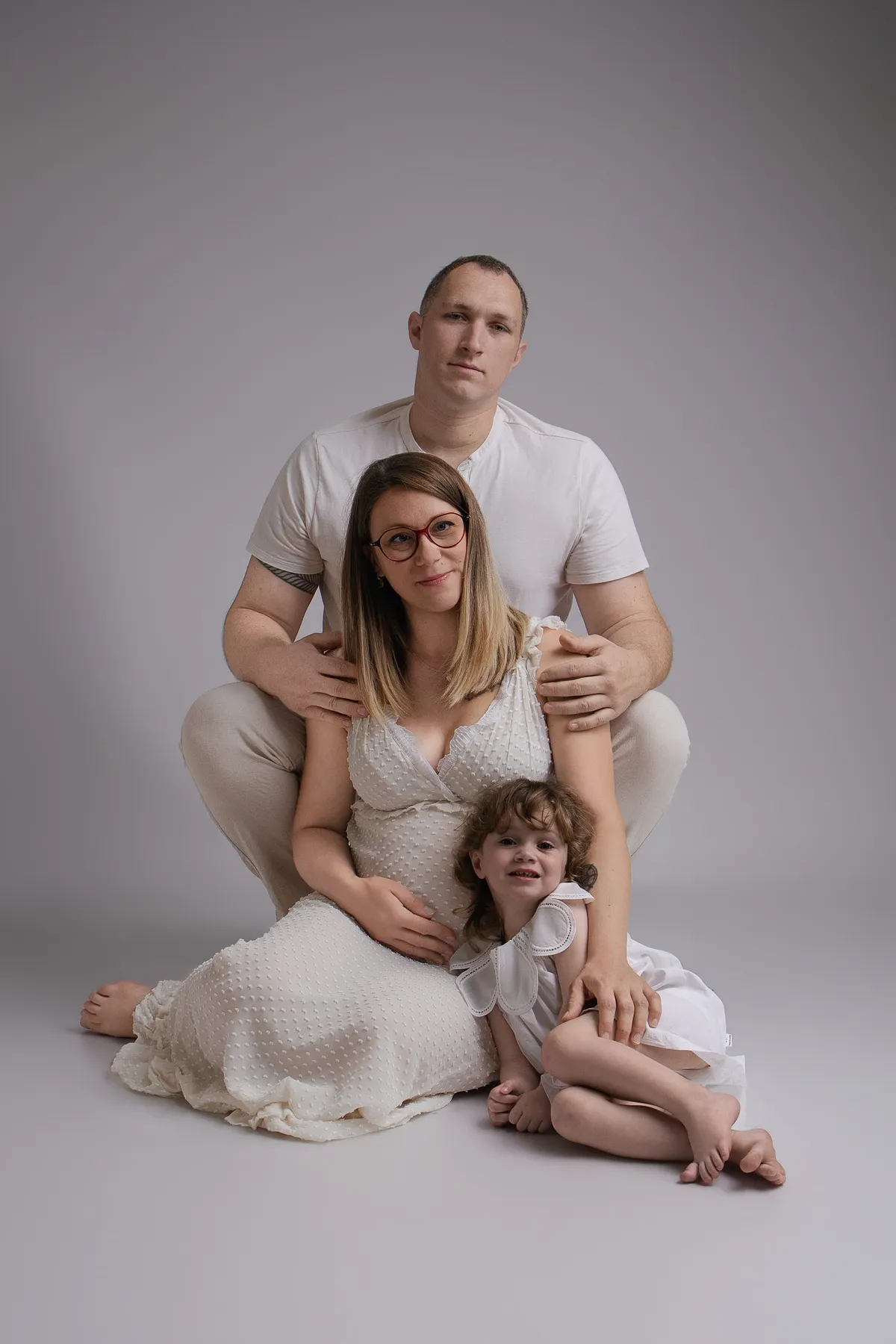 Famille en tenue claire autour d'une future maman et de sa fille, séance grossesse en studio - Cindy Poulet photographe