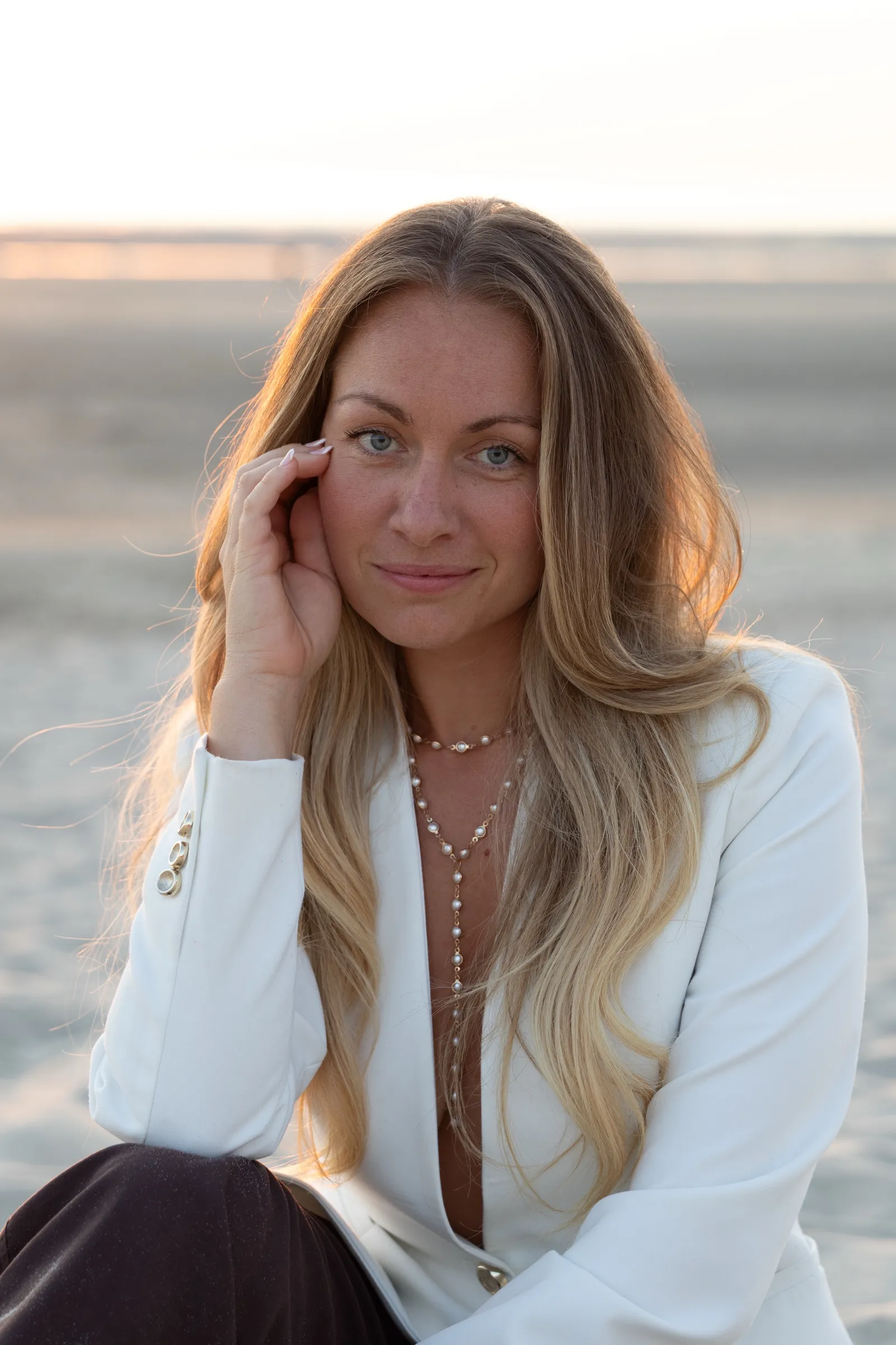 Portrait d'une femme en veste blanche sur la plage au coucher du soleil, lumière dorée - Cindy Poulet photographe