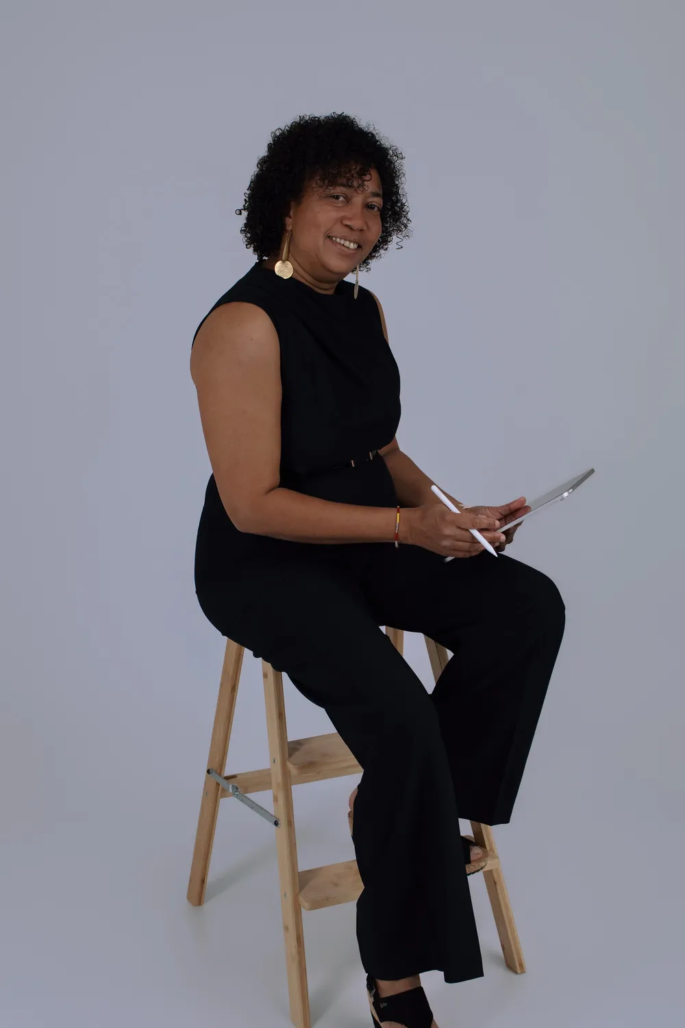 Femme souriante en combinaison noire assise sur un tabouret, tablette en main, portrait professionnel en studio - Cindy Poulet photographe
