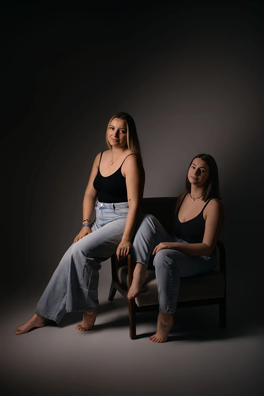Deux femmes dans un studio sombre, portrait duo en jean et haut noir - Cindy Poulet photographe