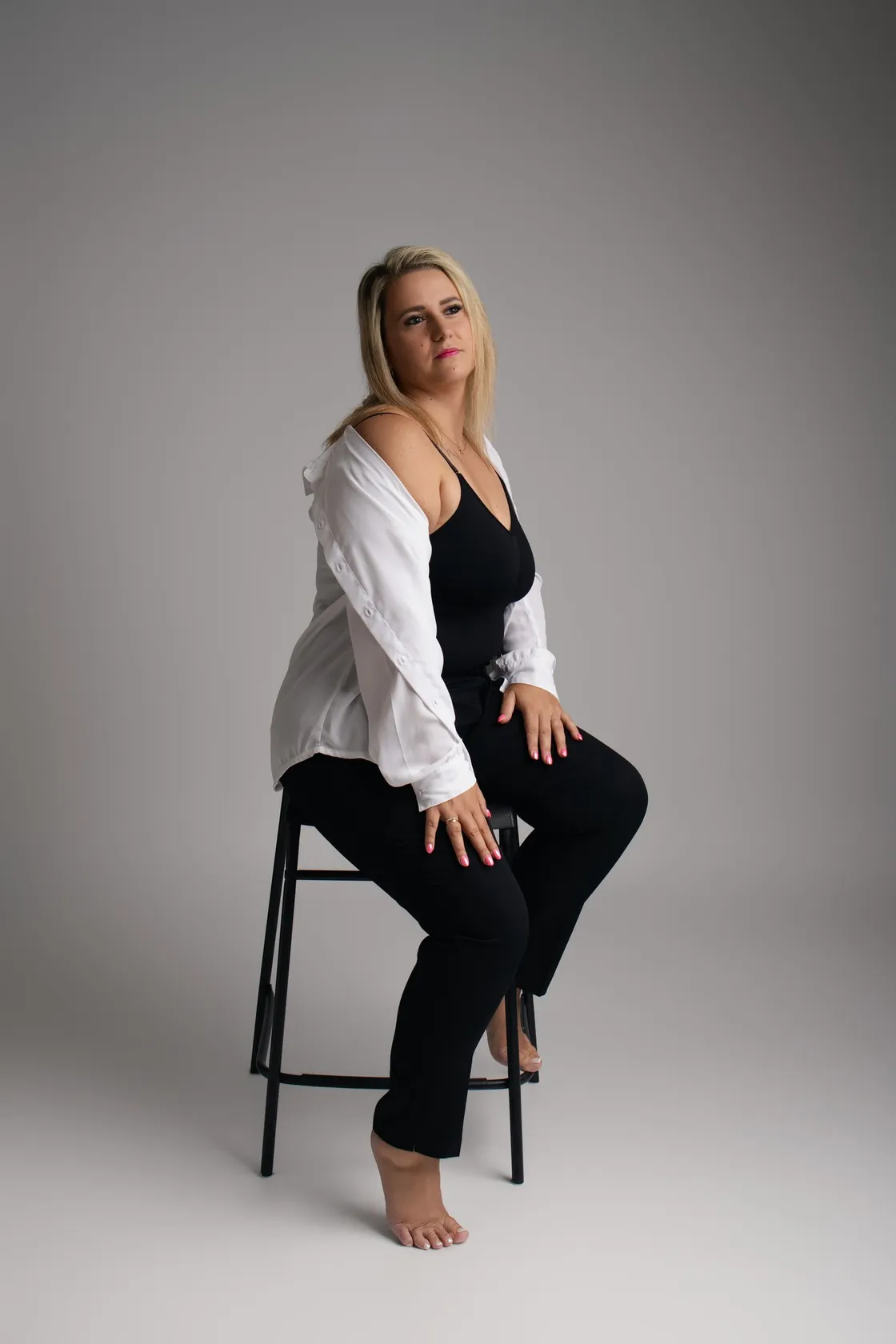 Portrait en studio d'une femme assise sur un tabouret, chemise blanche ouverte sur un débardeur noir - après retouche