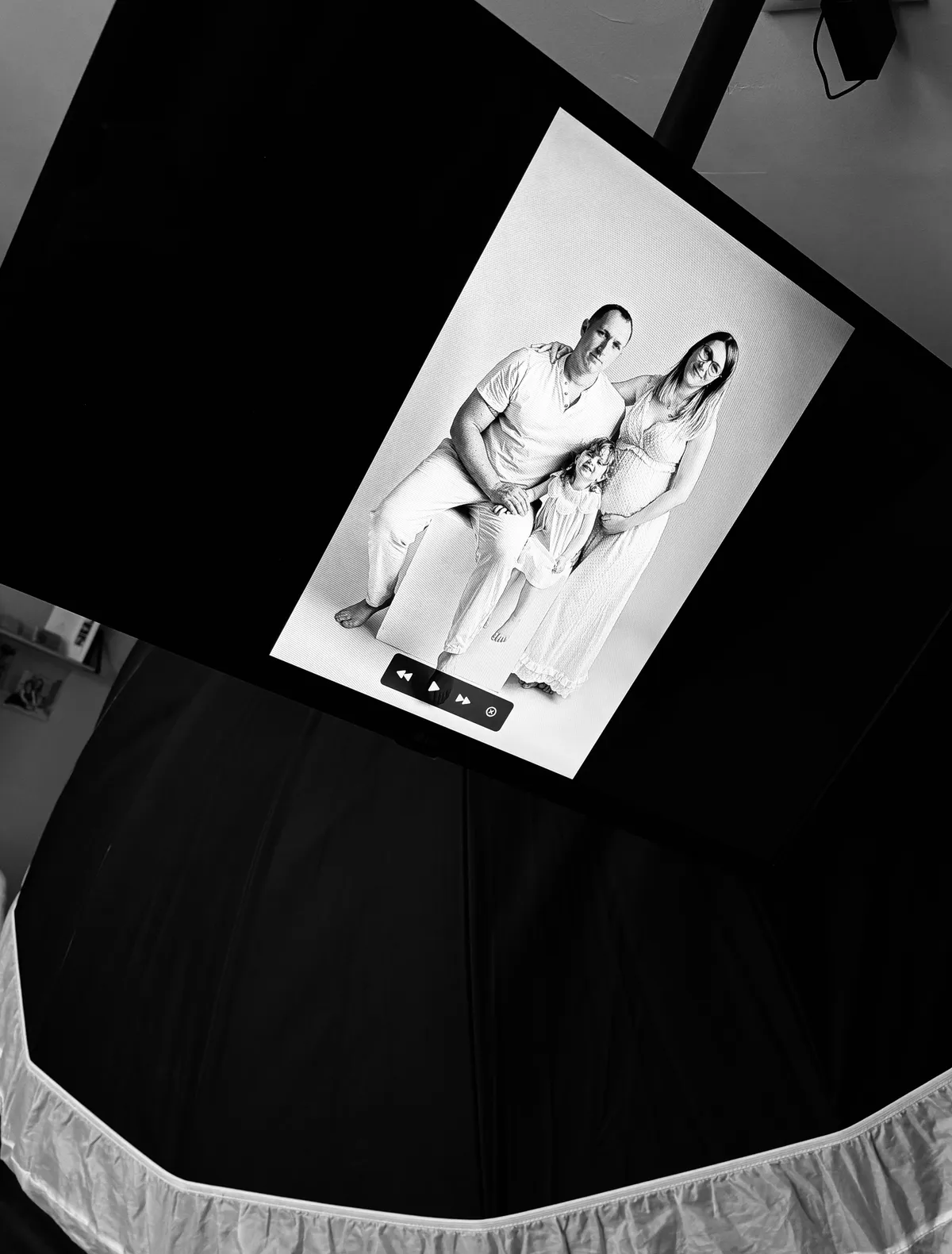 Visionnage des photos au studio : écran TV affichant un portrait de famille en noir et blanc juste après la séance.